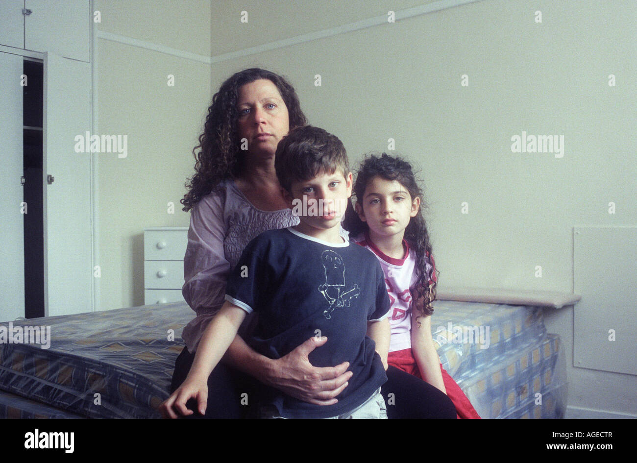 Eine schwangere alleinerziehende Mutter sitzt auf einem Bett mit ihren Kindern in ihr neues Zuhause, eine Wohnung in einer Sozialsiedlung. Mädchen im Alter von 9, jungen im Alter von 7. Stockfoto
