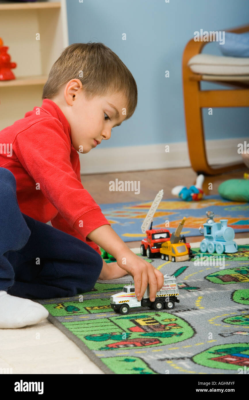 drei Jahre alte Junge spielt mit Spielzeug-LKW auf Matte mit Straßen und Häusern drauf Stockfoto