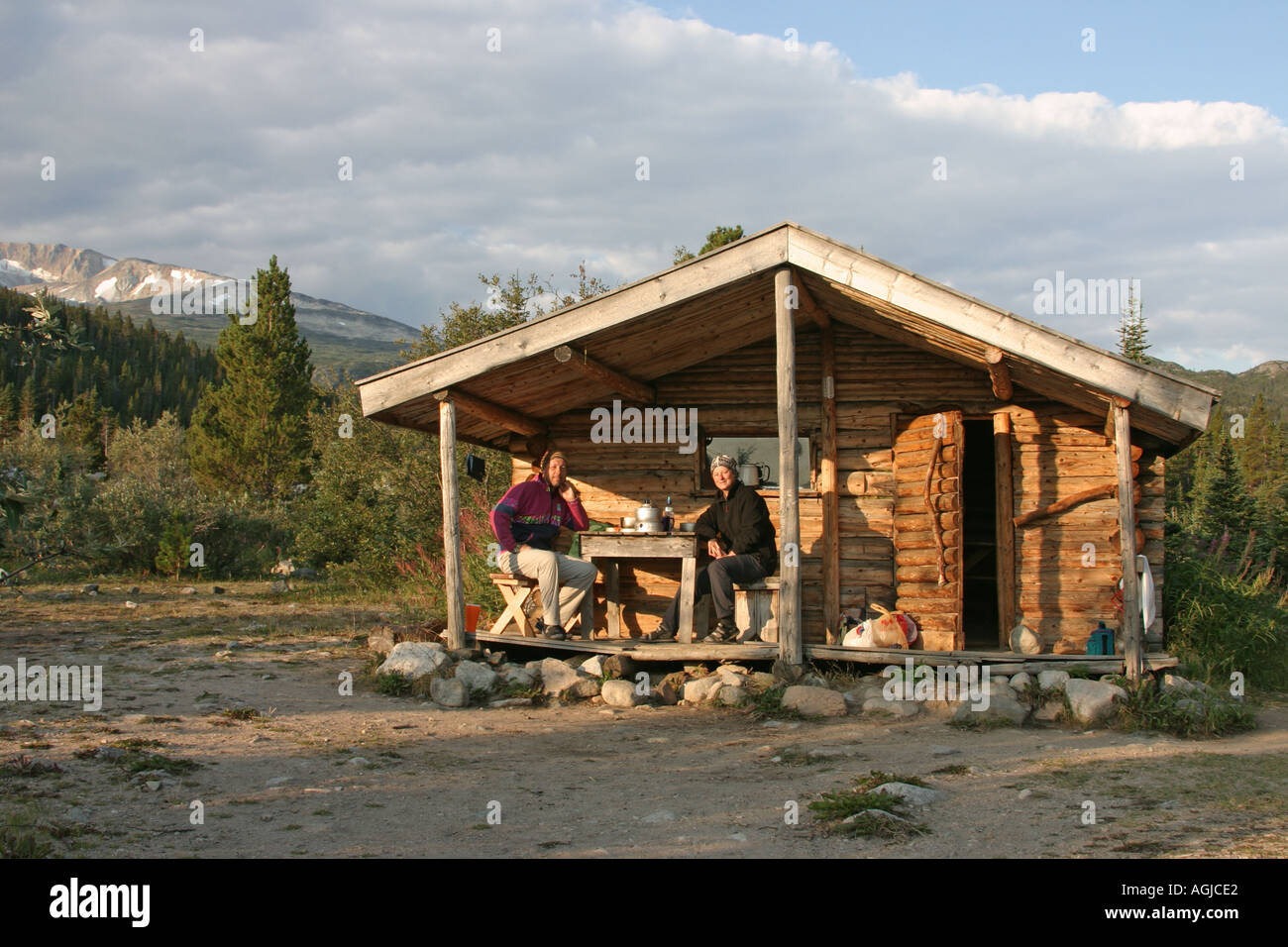 Herr paar sitzt unter dem Vordach eine gemütliche Blockhütte am See Lindemann Chilkoot Trail British Columbia Canada Stockfoto