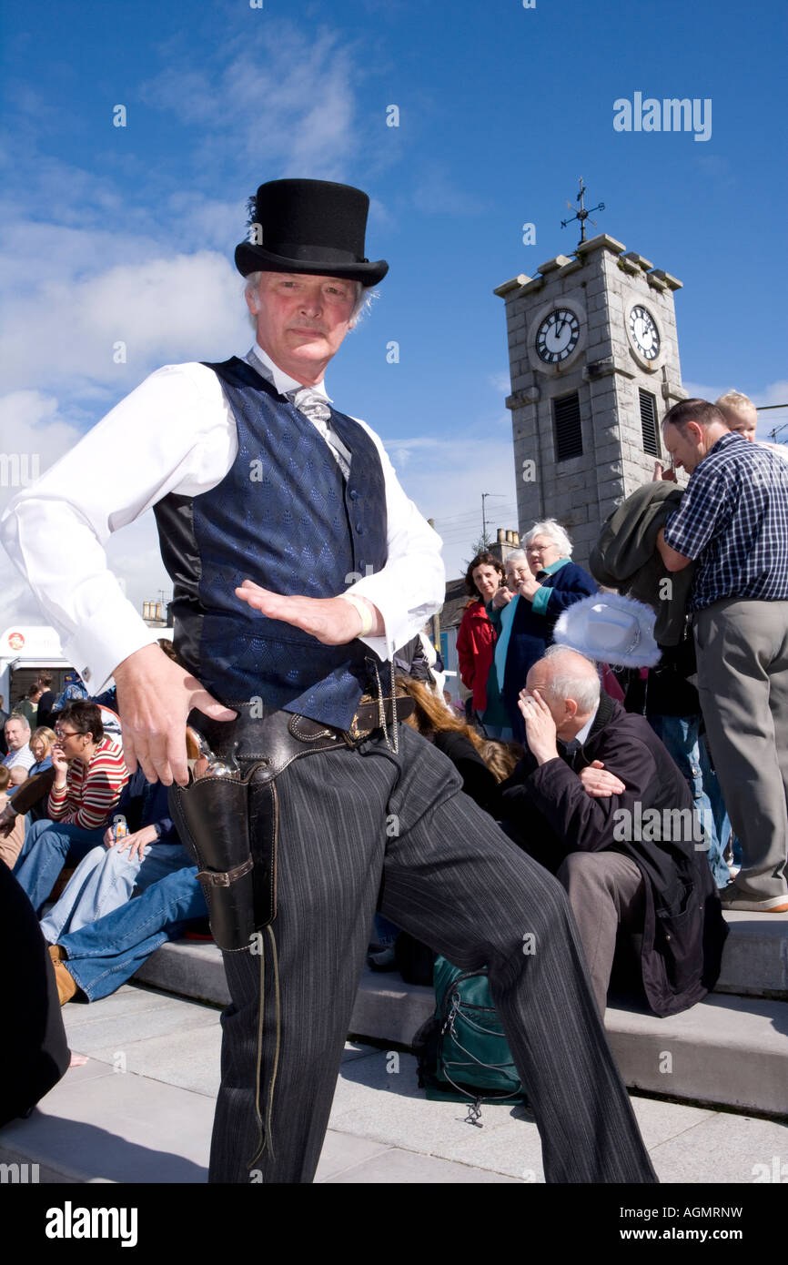 Schottische Veranstaltungen Creetown Country Music Festival Cowboy posiert mit Gewehr auf dem Platz mit Clocktower hinter Galloway Scotland UK Stockfoto