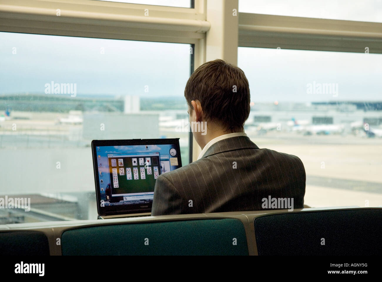 Mann auf dem Computer am Flughafen spielen Geduld auf seinem Laptop von Fenster Stockfoto