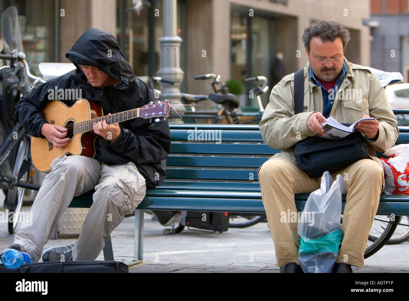 Ein Mann der Gitarre sitzt auf einer Bank neben einem Mann ein Buch Tour in Amsterdam Niederlande Stockfoto