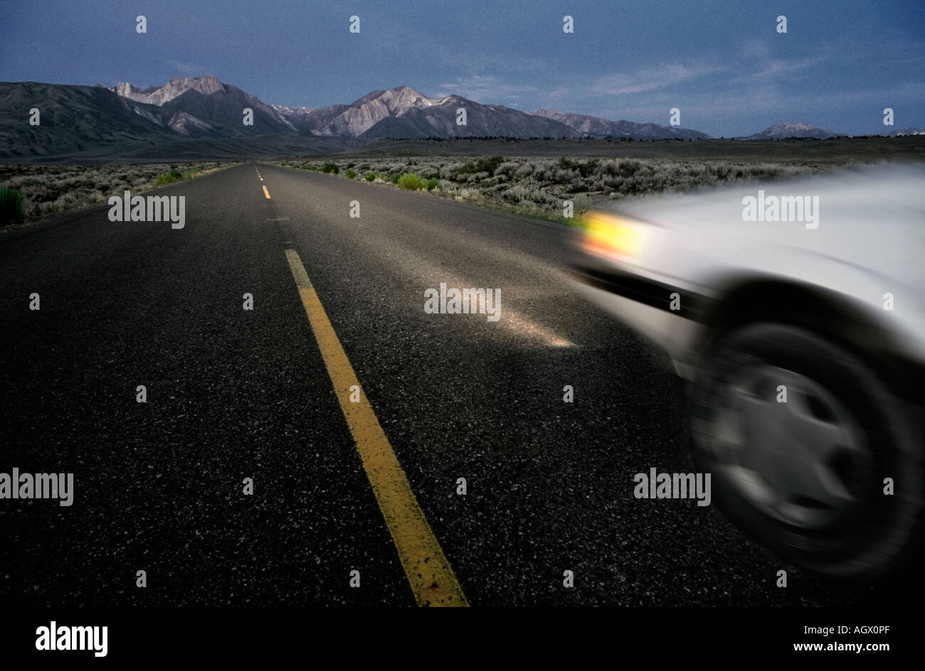 Ein Auto ist während der Nachtzeit in einem Tal in der Nähe der Berge fahren entlang einer Autobahn abdunkeln verschwommen. Stockfoto