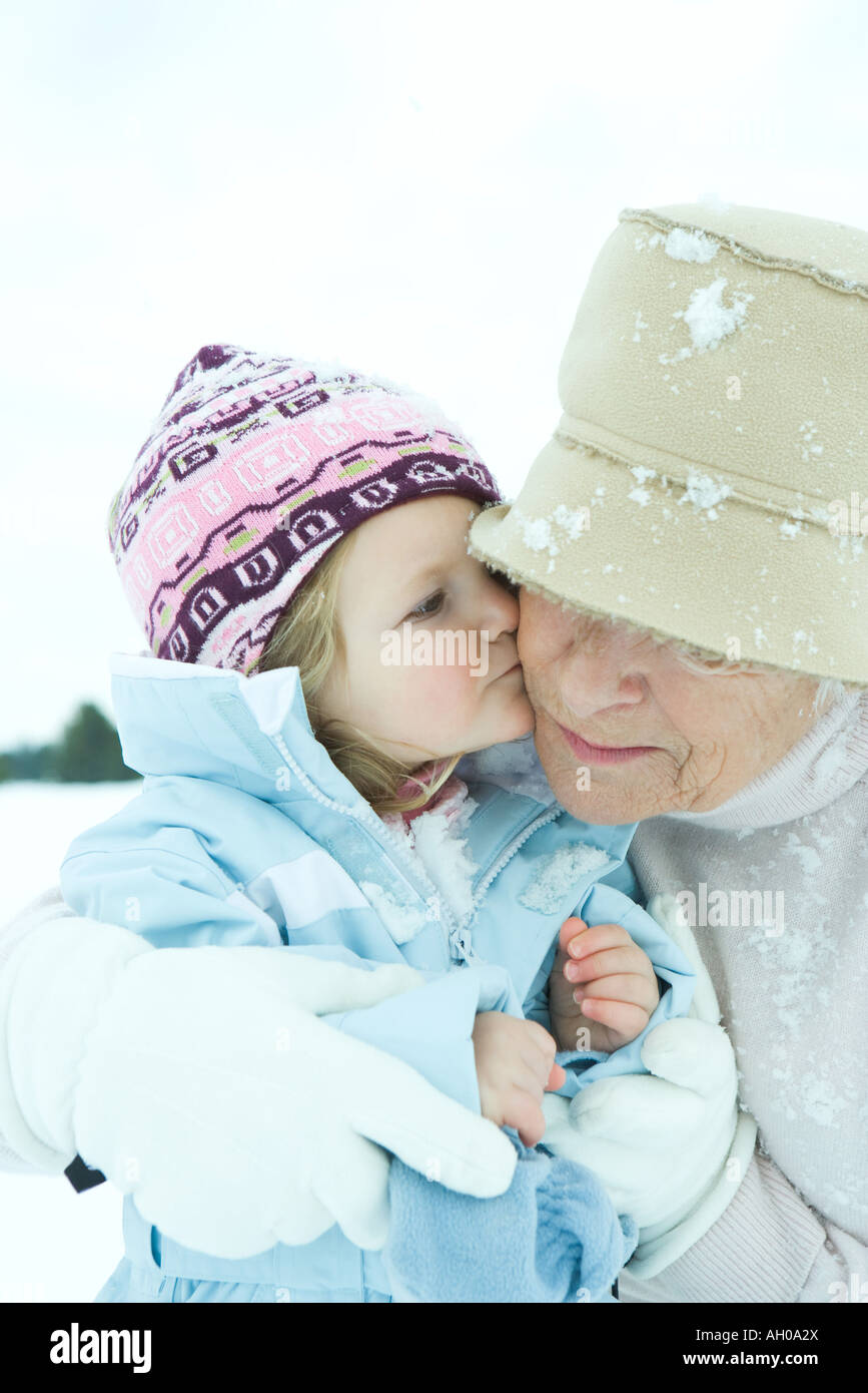 Kleinkind Mädchen küssen Großmutter auf Wange im Schnee, Nahaufnahme Stockfoto