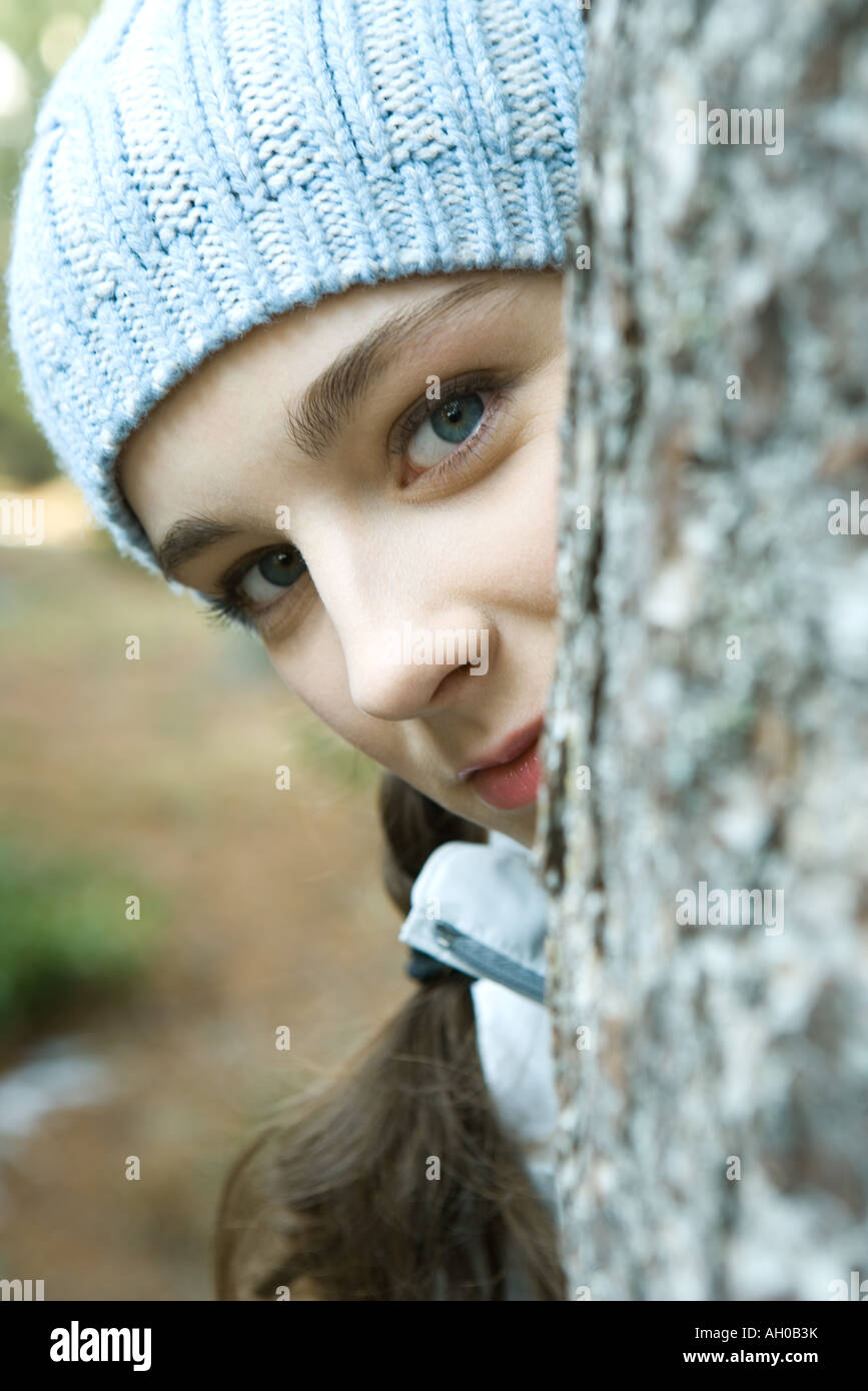 Teenager-Mädchen spähen um Baumstamm, Blick in die Kamera, Porträt Stockfoto