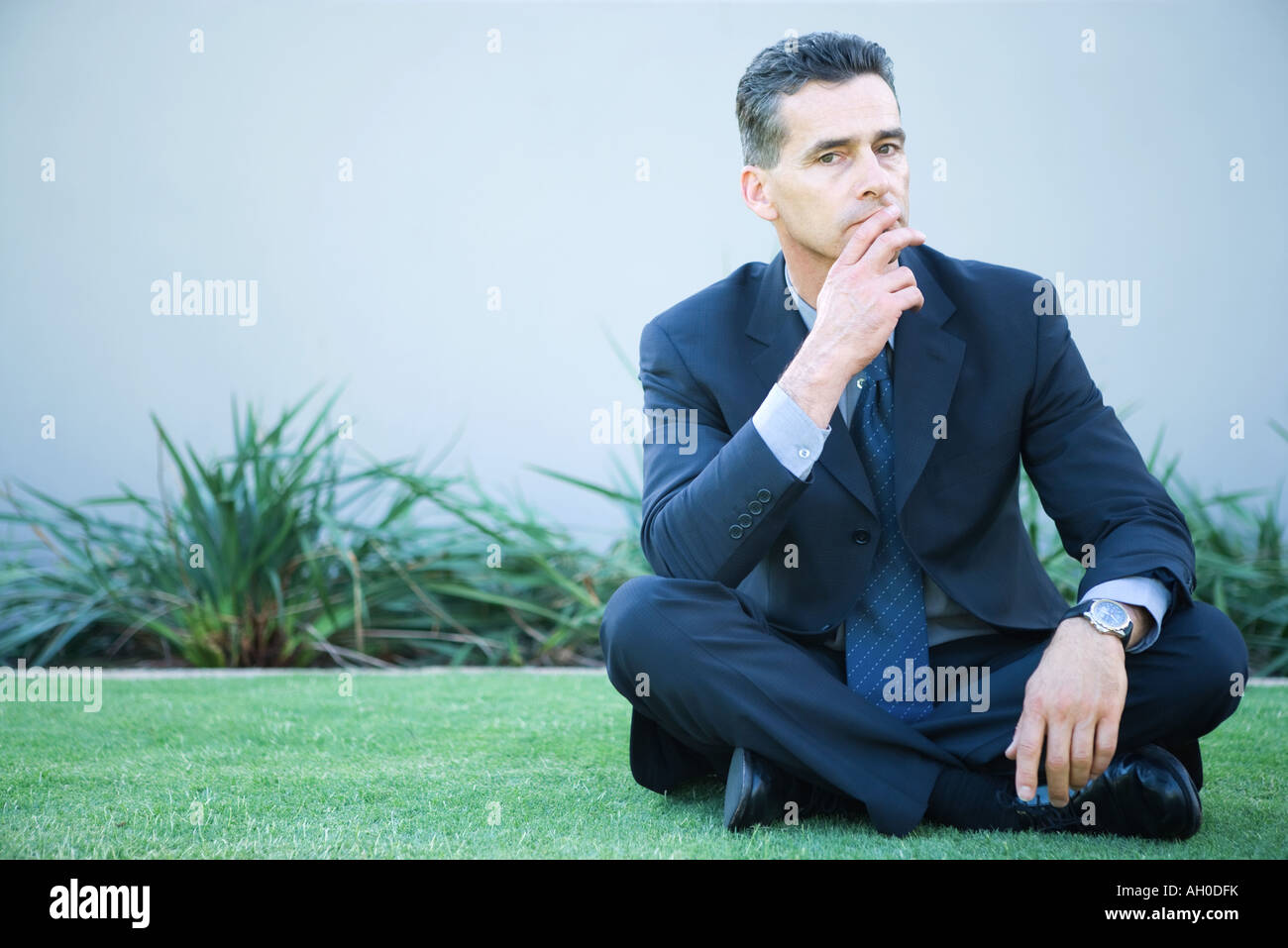Geschäftsmann, sitzen mit gekreuzten Beinen auf dem Rasen, Finger über die Lippen Stockfoto