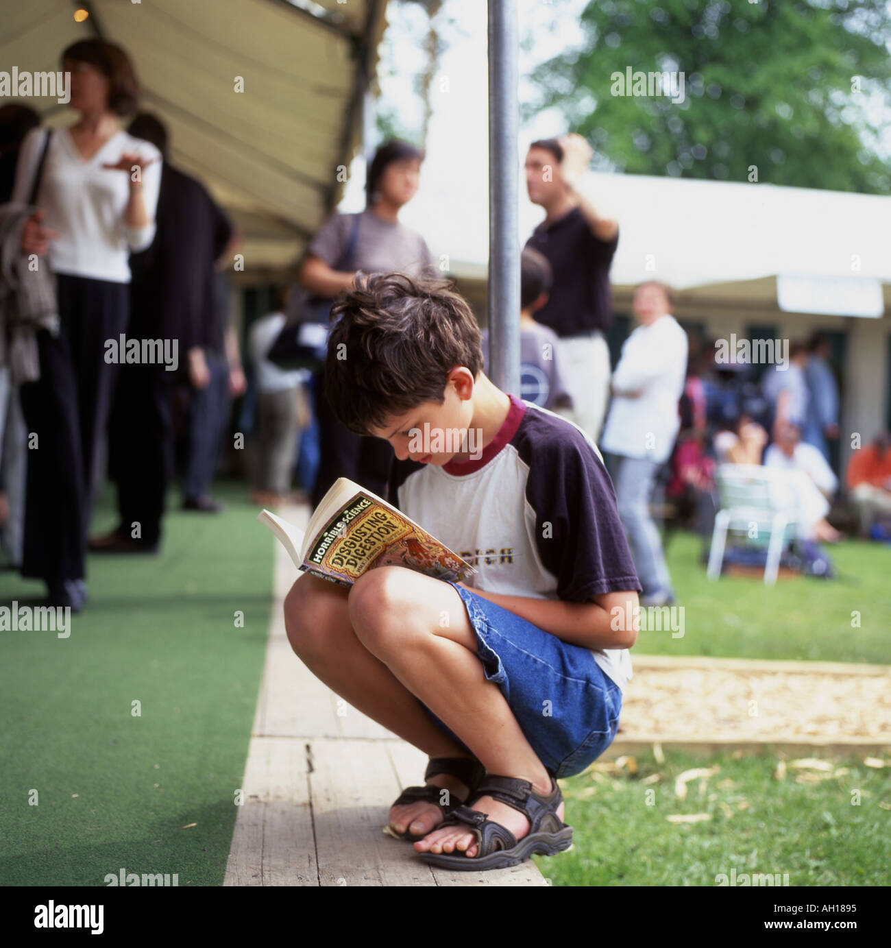 Ein kleiner Junge hockt beim Lesen der schrecklichen Wissenschaft 'Verdauung' halten Ein Buch auf dem Hay Festival in Wales UK KATHY DEWITT Stockfoto