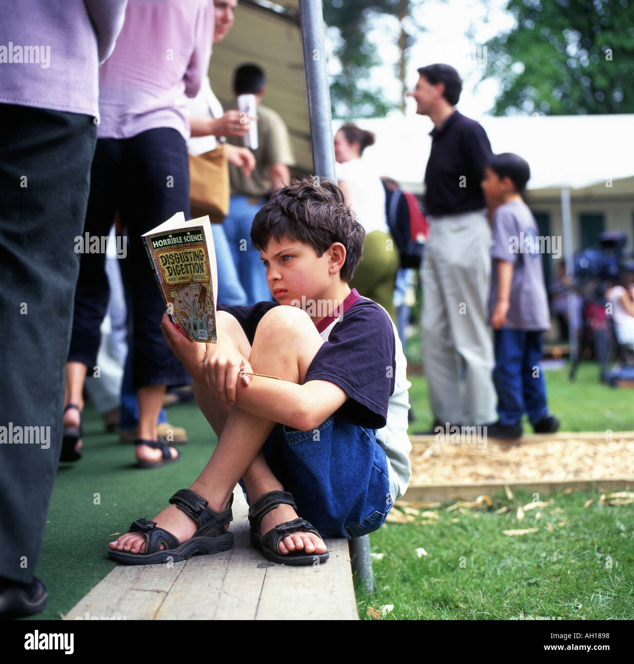 Ein junger Junge sitzt ein Buch aus der schrecklichen Science-Serie in einer Warteschlange beim Hay Festival, Hay on Wye, Wales UK KATHY DEWITT lesen Stockfoto