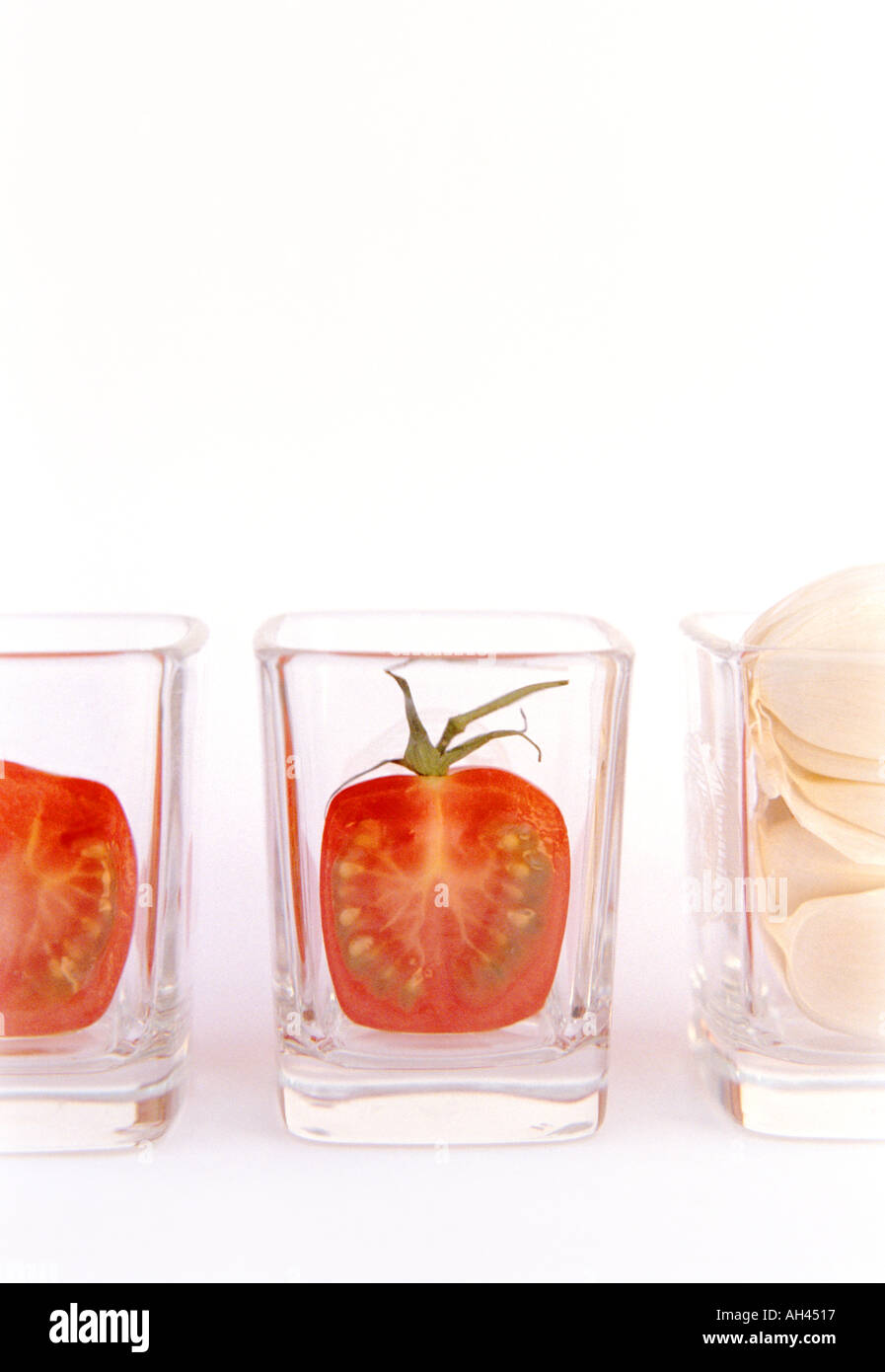 Mini-Kirschen-Tomaten in Scheiben geschnitten und Knoblauchzehe in sauberes Glas shot Gläser auf weißem Hintergrund vertikal aufgereiht Stockfoto