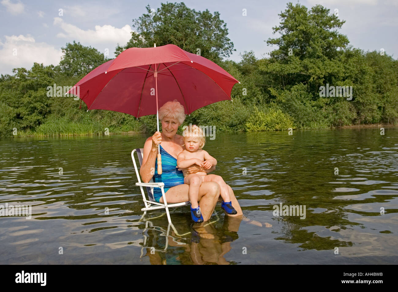Oma und Baby-sitting auf Picknick Stuhl im Fluss Wye Holding roten Regenschirm Abkühlung an heißen Tagen UK Stockfoto