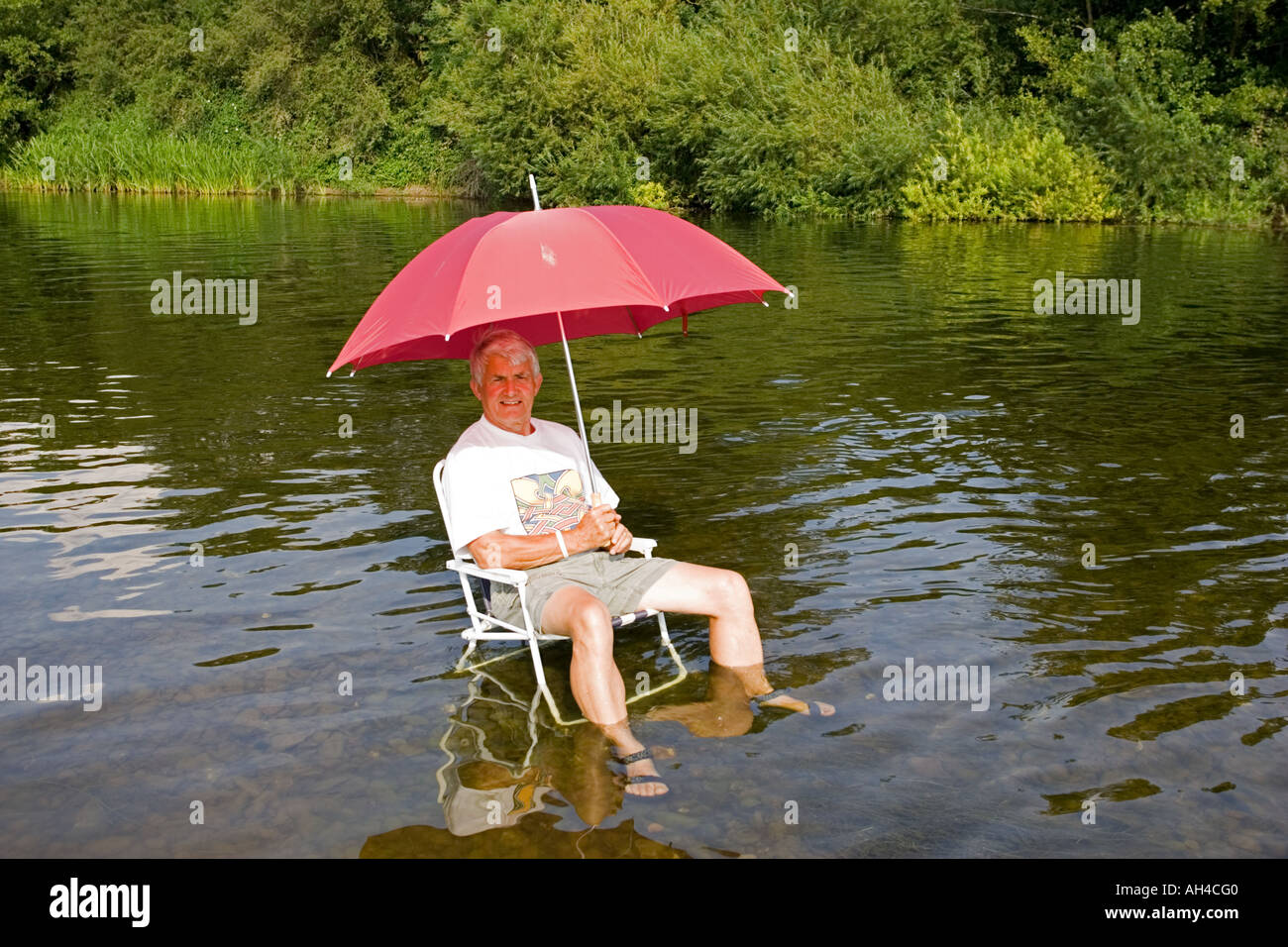Mann mit roten Regenschirm auf Picknick Stuhl kühl zu halten im Fluss Wye an heißen Tag UK Stockfoto