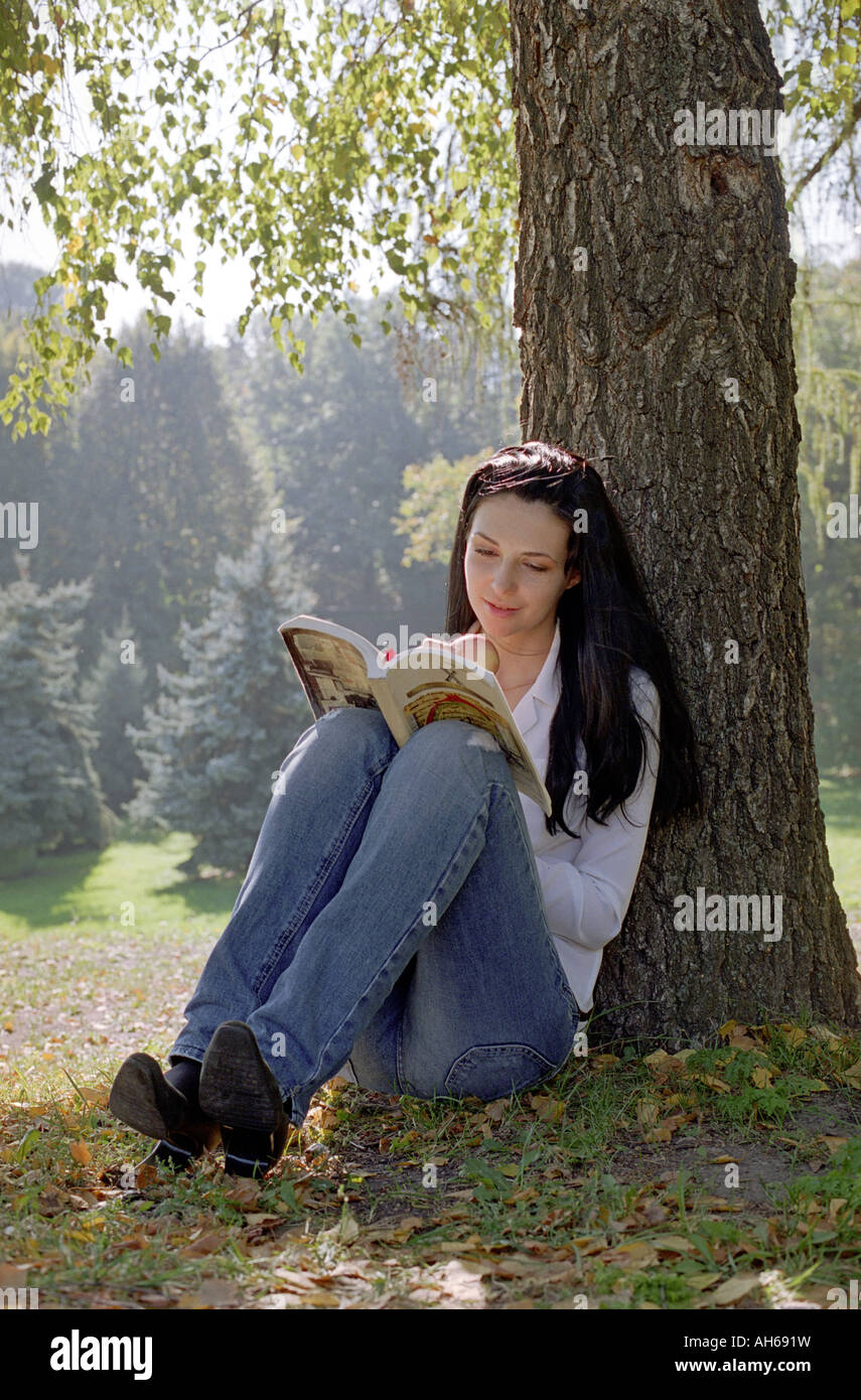 Lesende Frau sitzen unter Baum Stockfoto