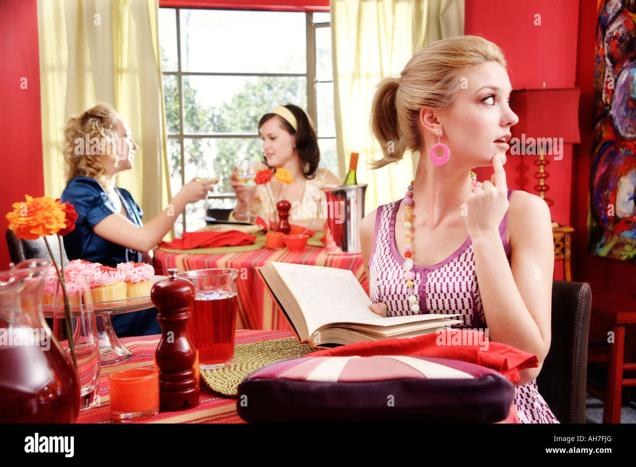 Junge Frau hält ein Buch mit zwei jungen Frauen Essen in einem Restaurant hinter ihr Stockfoto
