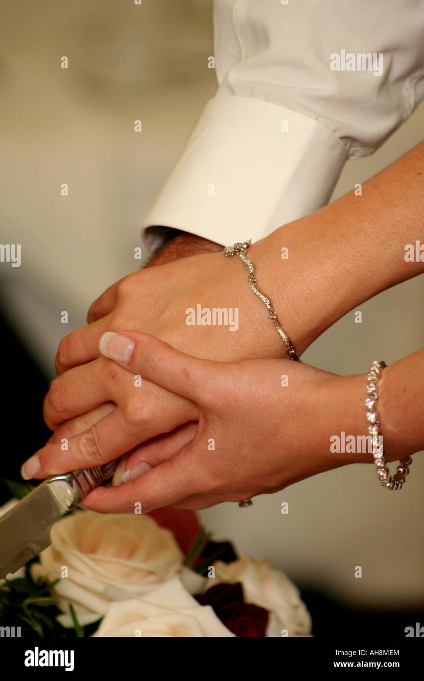 Braut und Bräutigam halten Sie Hände, wie sie ihre Hochzeitstorte zu schneiden Stockfoto