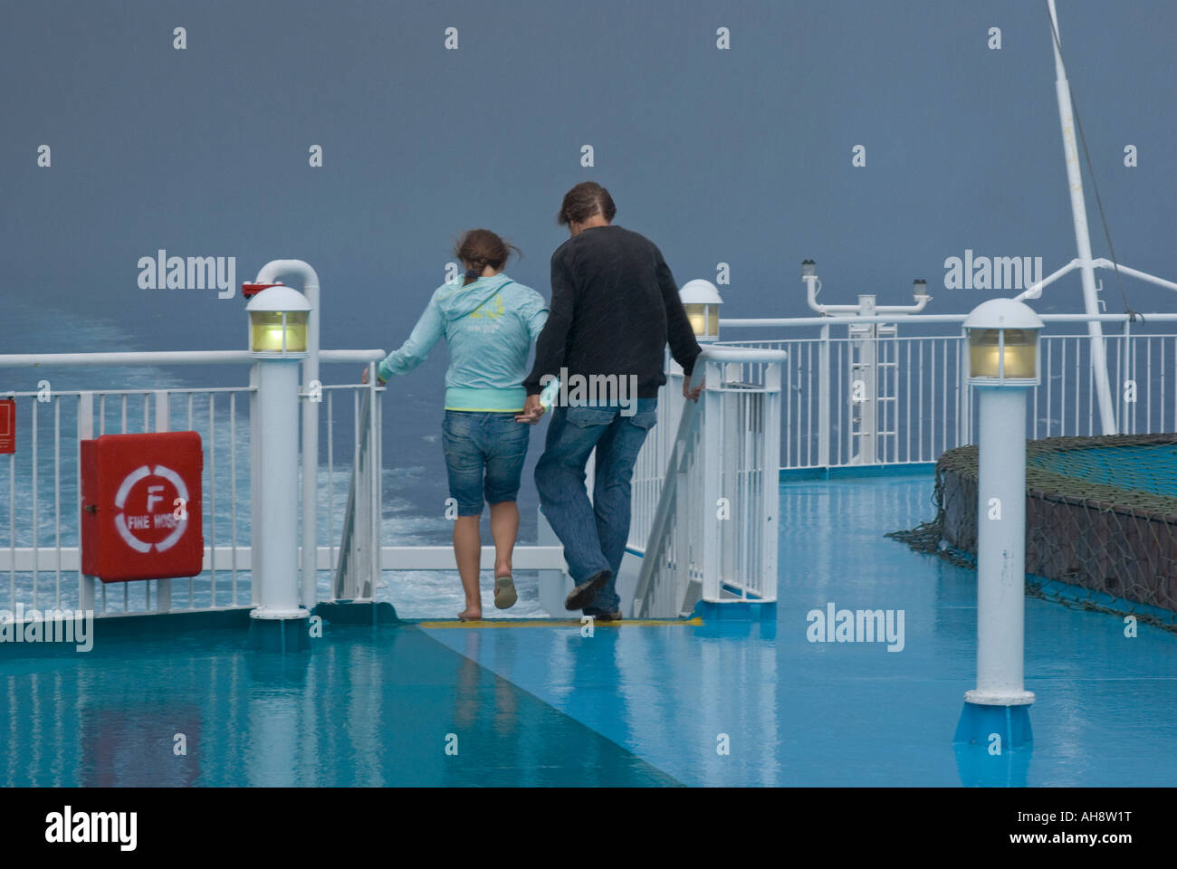 ein paar Passagiere an einem regnerischen Tag auf dem Außendeck einer Fähre unter stürmischem Wetter Stockfoto