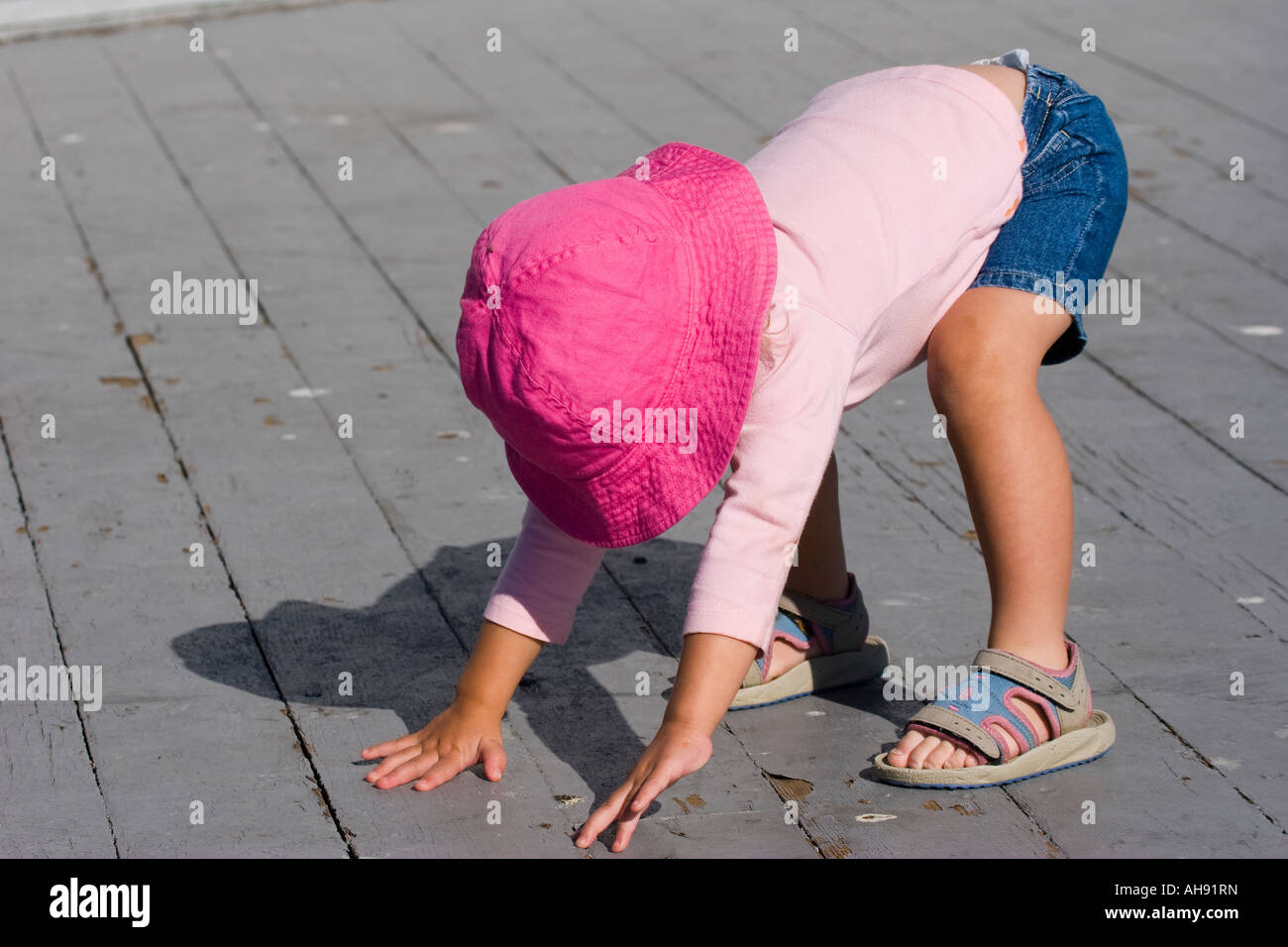 Zwei Jahre altes Mädchen in einem rosa Top und Hut bücken und drücken sich in eine stehende position Stockfoto
