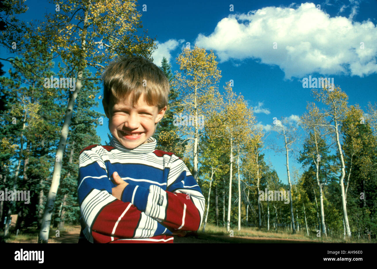 Fröhlicher Junge vor aspen Wald tragen Rollkragenpullover auf einen warmen Sommer- oder Herbsttag Kind ist ca. 7-8 oder 9 Jahre alt Stockfoto
