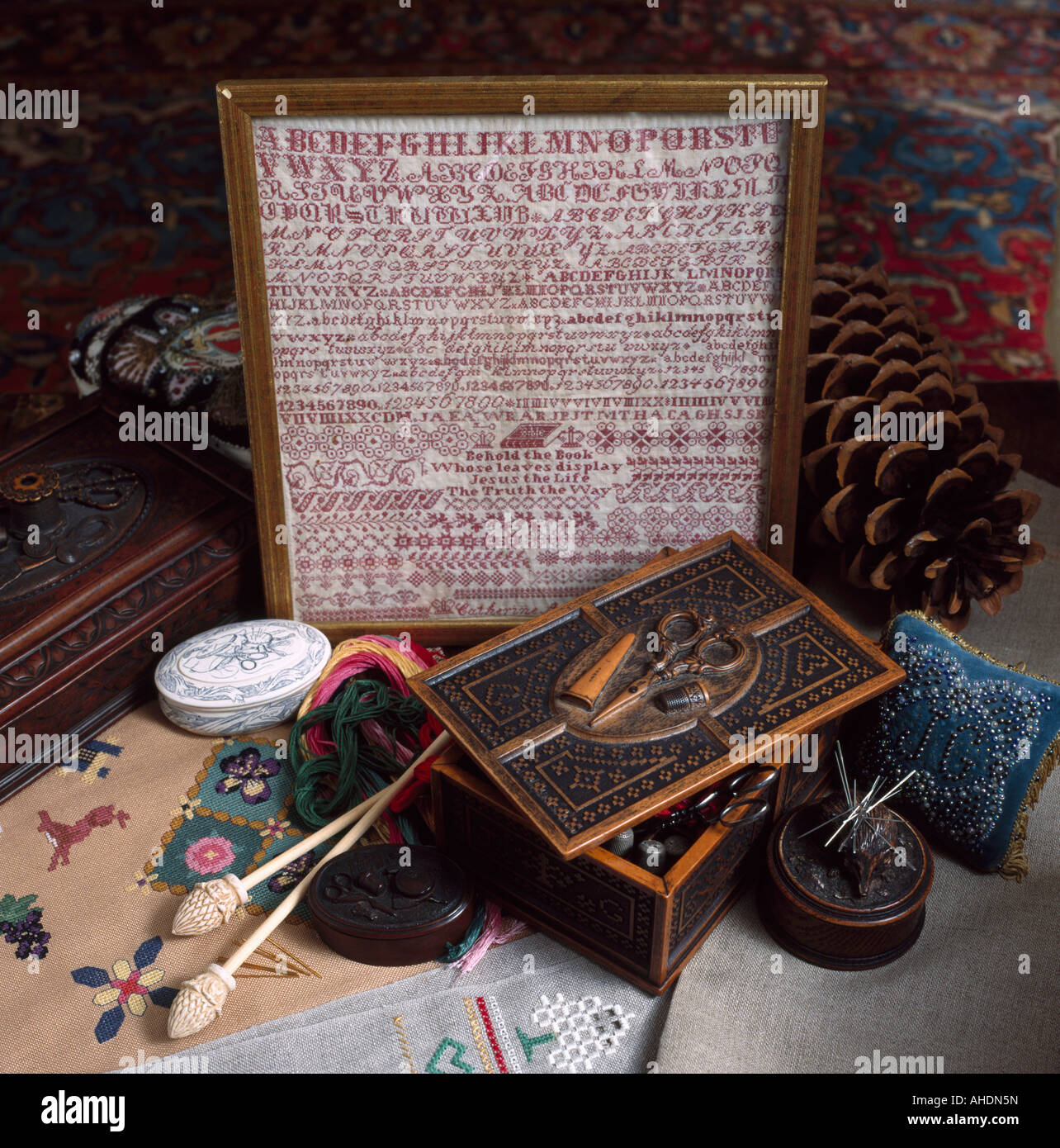 Nahaufnahme von gerahmten antiken Sampler und alte geschnitzte Holzkiste mit Nähen Materialien Stockfoto