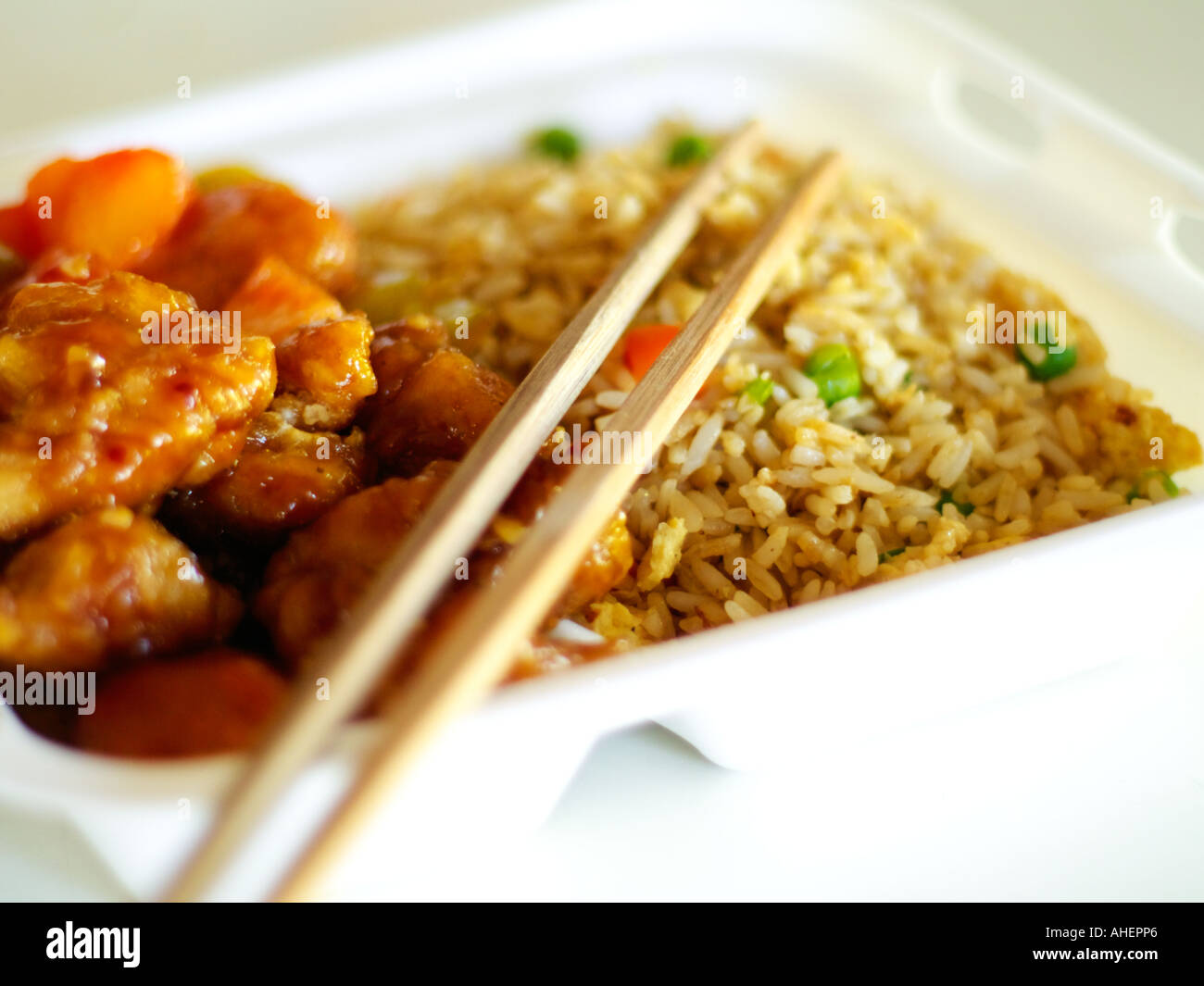 Chinesisches Essen zum Mitnehmen (General Tso Chicken und gebratener Reis) in weißem Styropor mit Bambus Stäbchen im flachen Fokus. Stockfoto