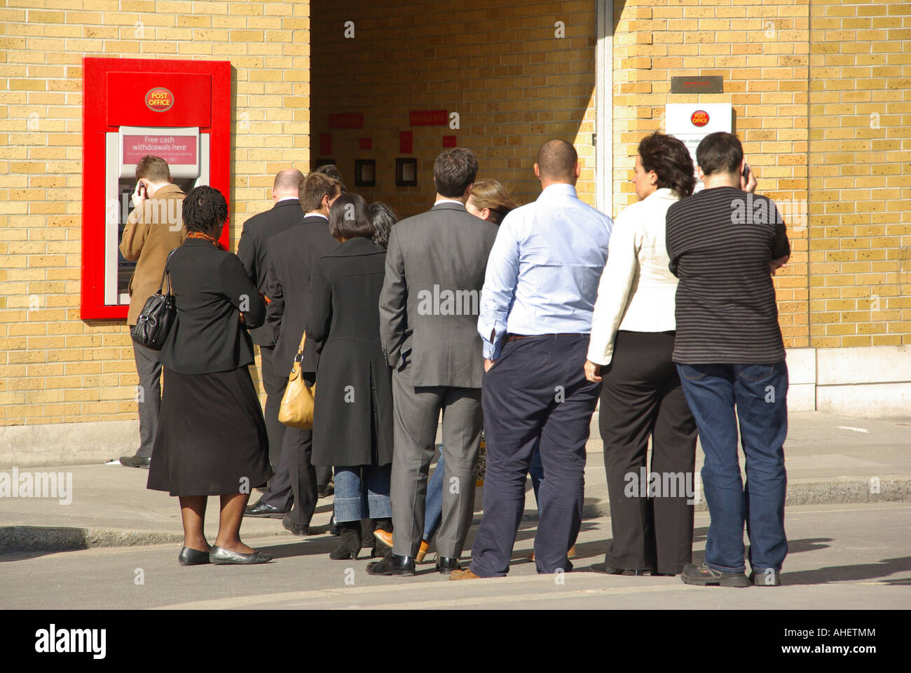 Mittagspause Warteschlange Zurück Ansicht Menschen warten auf ihr Geld aus Loch in der Wand Geldautomat vor der Post Office City of London England Großbritannien abzuheben Stockfoto