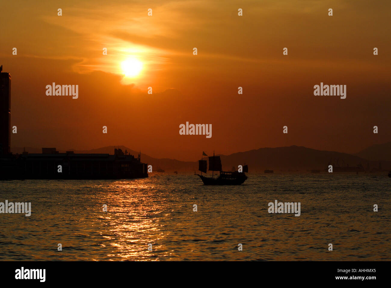 Alte chinesische Dschunke vor einem goldenen roten Sonnenuntergang in Victoria Harbour, Hongkong Stockfoto