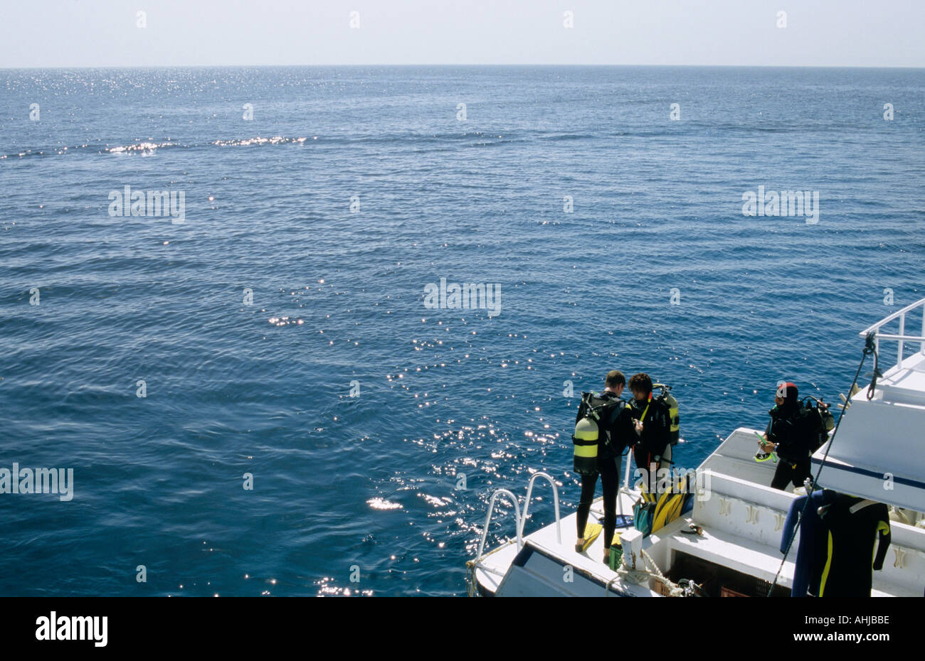 Zwei Taucher überprüfen die Ausrüstung an Bord eines Tauchboots, bevor sie einen Tauchgang beginnen, während ein dritter Taucher auf sie schaut. Hurghada, Ägypten. Stockfoto