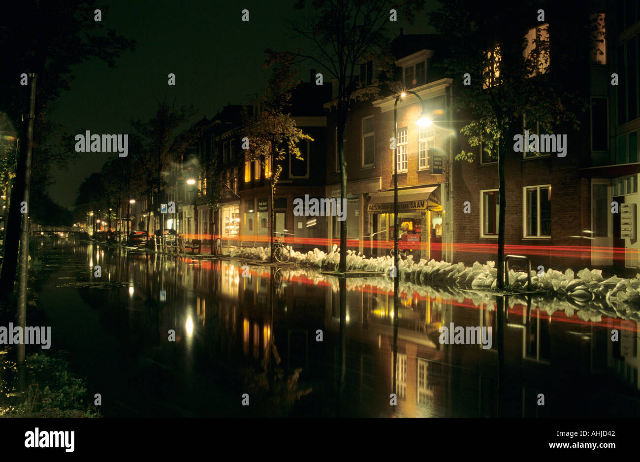 Kanal in der Nacht mit Sandsäcken an den Ufern, um Überschwemmungen zu verhindern. Häuser und Geschäfte gegenüber mit verschwommener Heckbeleuchtung vor dem Hotel. Delft, Niederlande. Stockfoto