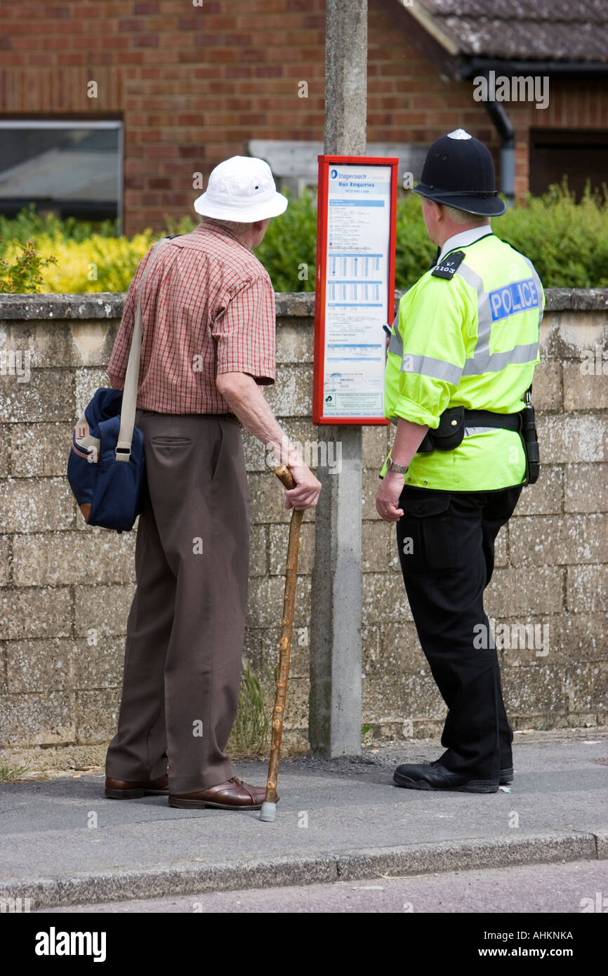 Lokale Polizei Polizist hilft einen älteren Mann warten an der Bushaltestelle Stockfoto
