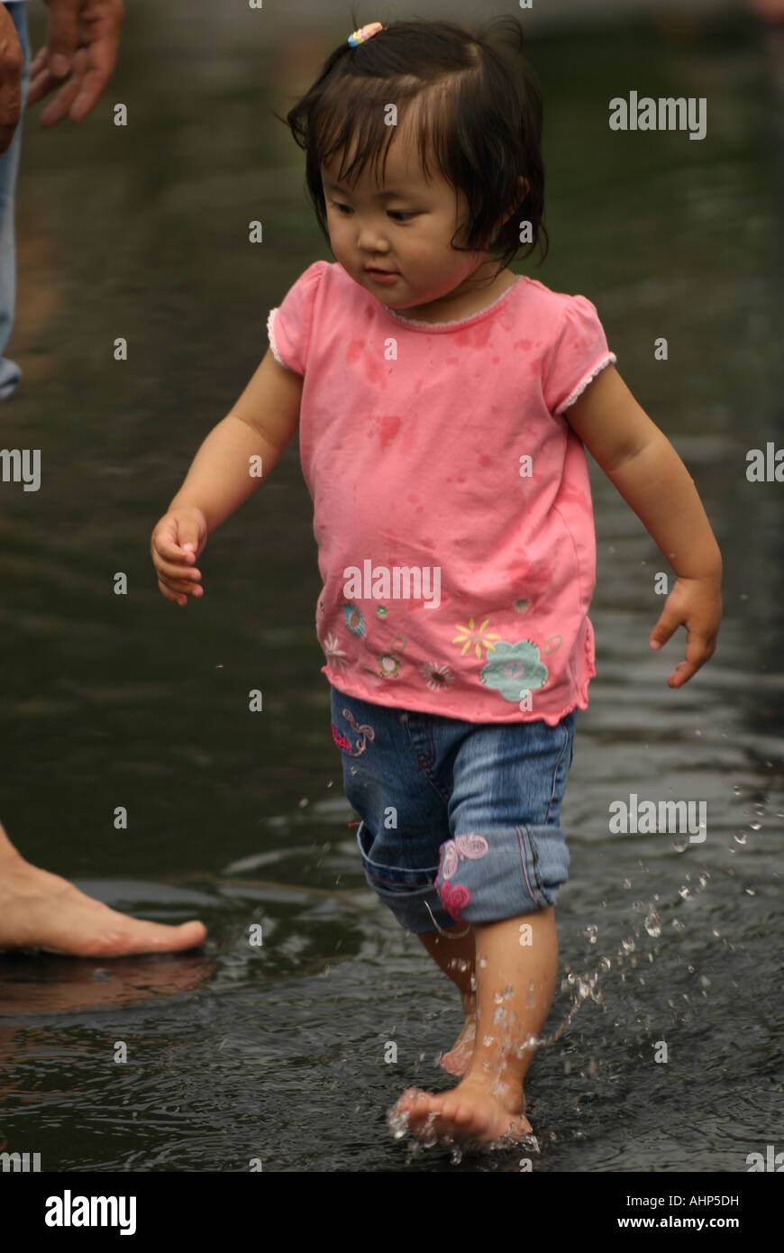 Eine kleine Asiatin in einem rosa t-Shirt spritzt in einen öffentlichen Brunnen Stockfoto