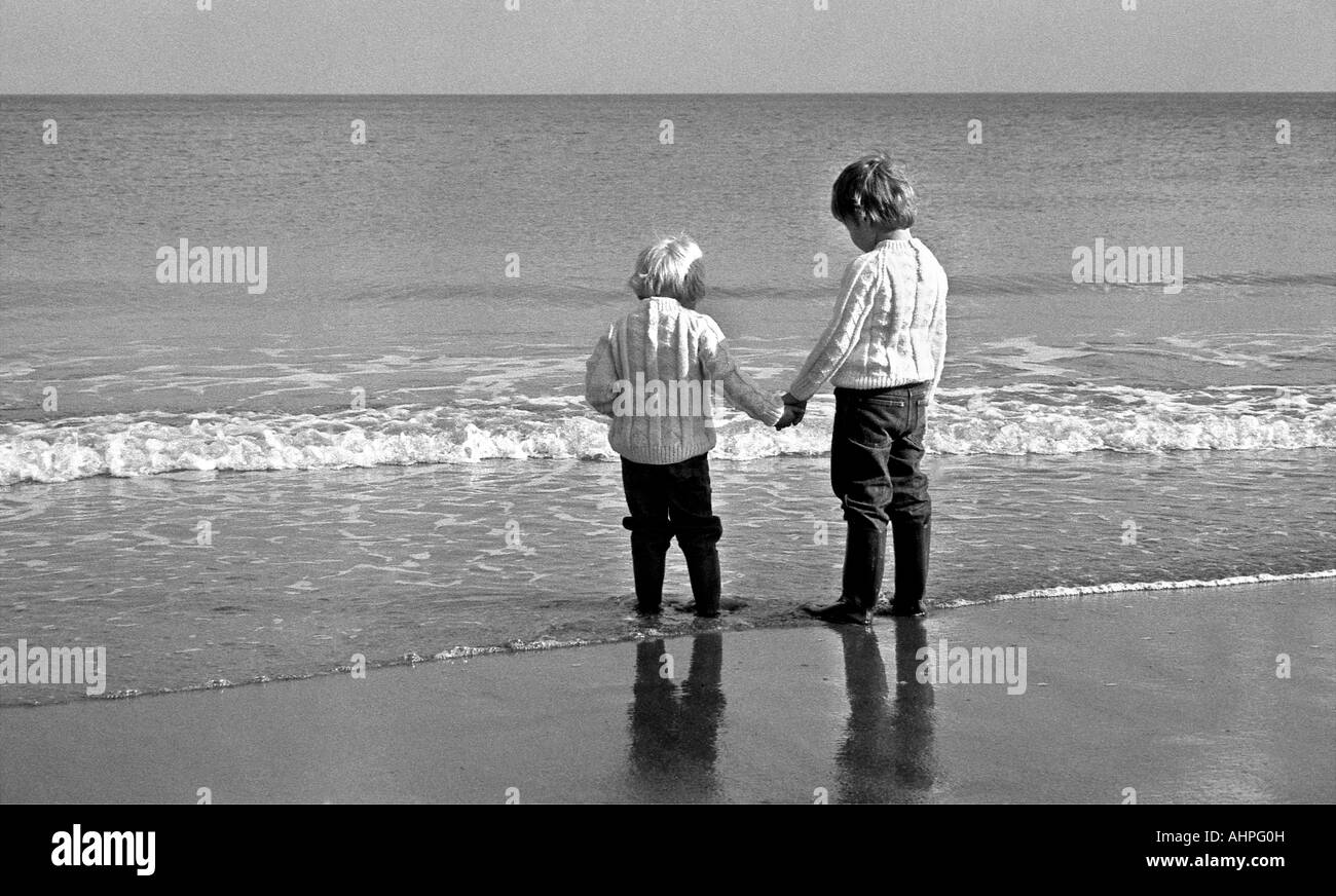 Zwei kleine Jungs an einem Strand am Rand Wassers an einem hellen Tag im Winter. Stockfoto