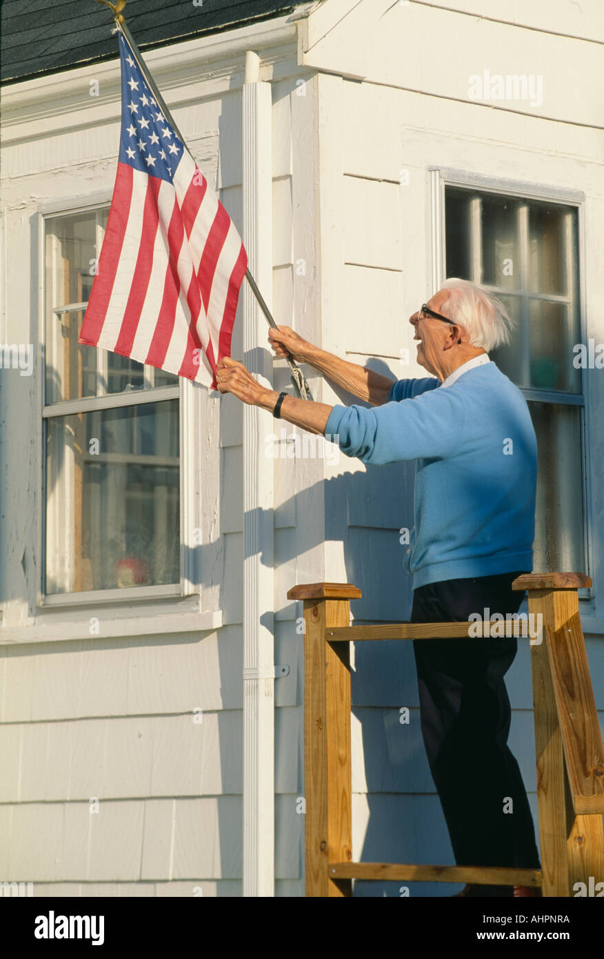 Senioren, die Anhebung der amerikanischen Flagge auf Haus in Stonington Maine Stockfoto