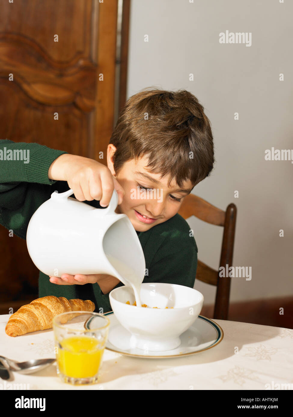 Jungen (6-8) Gießen Milch über Müsli zum Frühstück Stockfoto