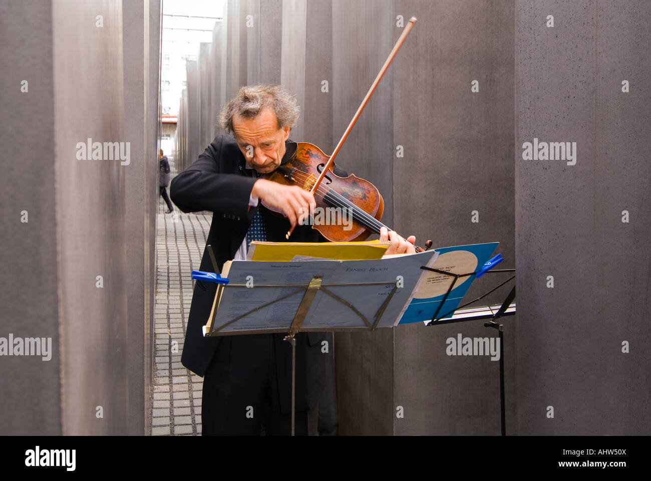 Horizontale Nahaufnahme eine Sologeiger spielen düstere Musik dazwischen die Steinen des Holocaust-Mahnmals an einem sonnigen Tag. Stockfoto