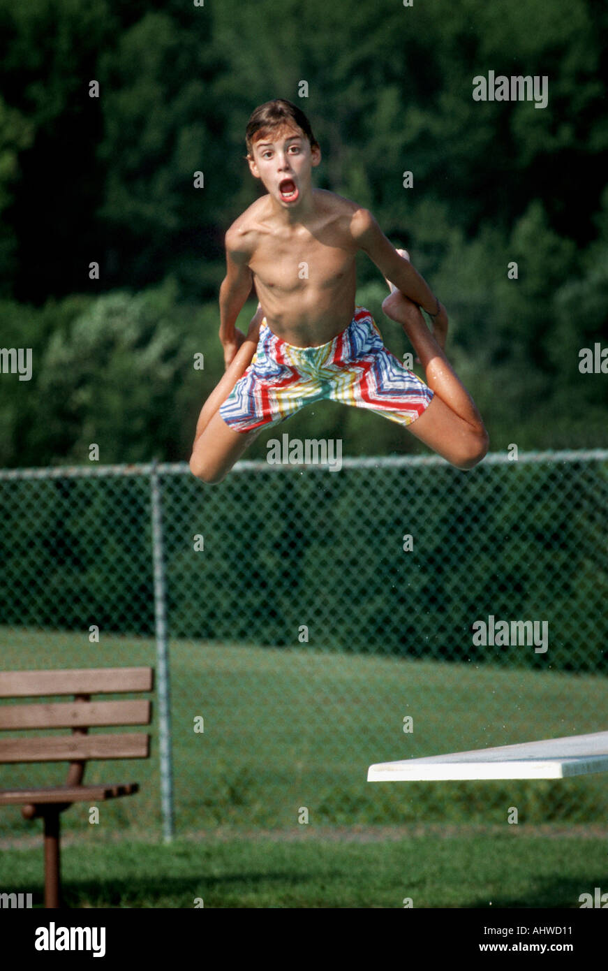 12 Jahre alter Junge aus zeigt, wie er von einem Sprungturm in einem öffentlichen Schwimmbad springt Stockfoto