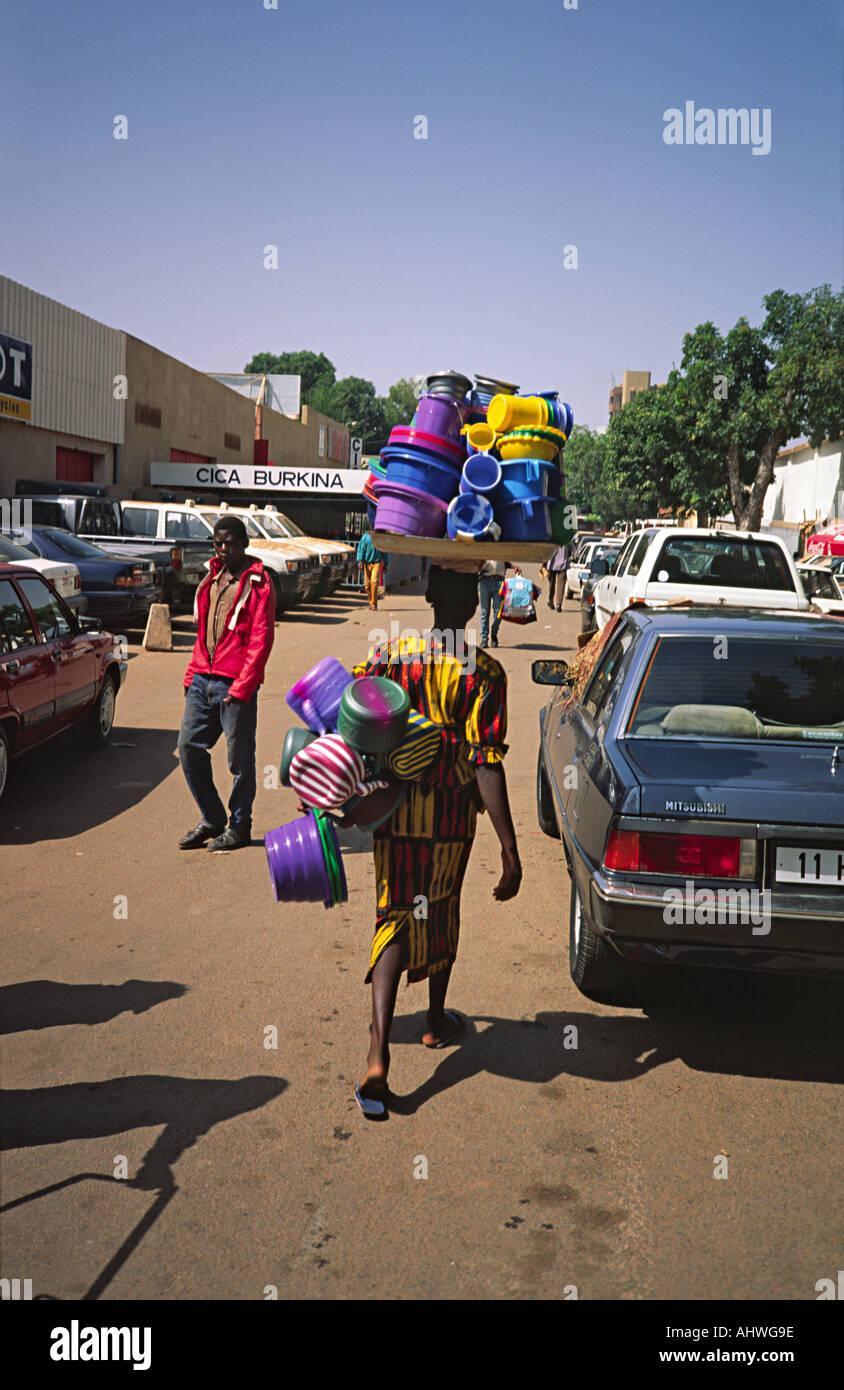 Weibliche Street Verkäuferin zu Fuß mit Kunststoff-Küche Waren auf ihrem Kopf. Ouagadougou, Burkina Faso Stockfoto