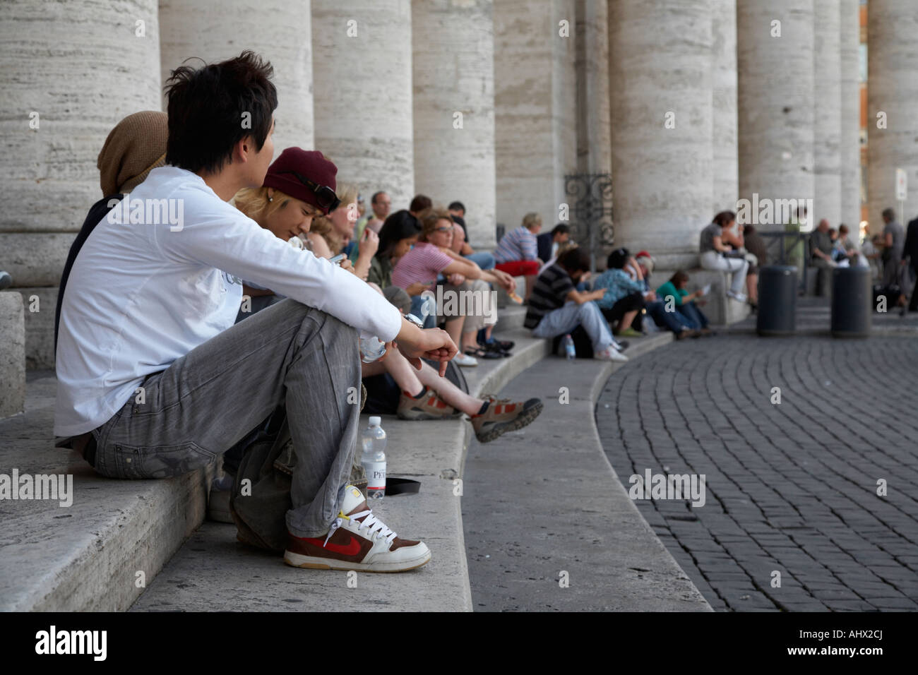 Touristen sitzen im Schatten auf den Stufen der Kolonnade St. Peters Platz Vatikanstadt Rom Stockfoto