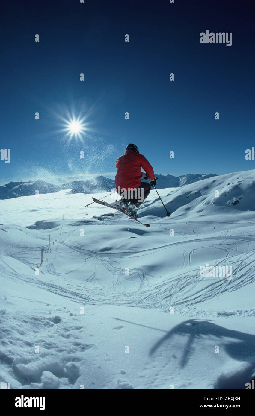 Skifahrer, die über einen Sprung mit Moutainrange und Sonne vor ihm Stockfoto