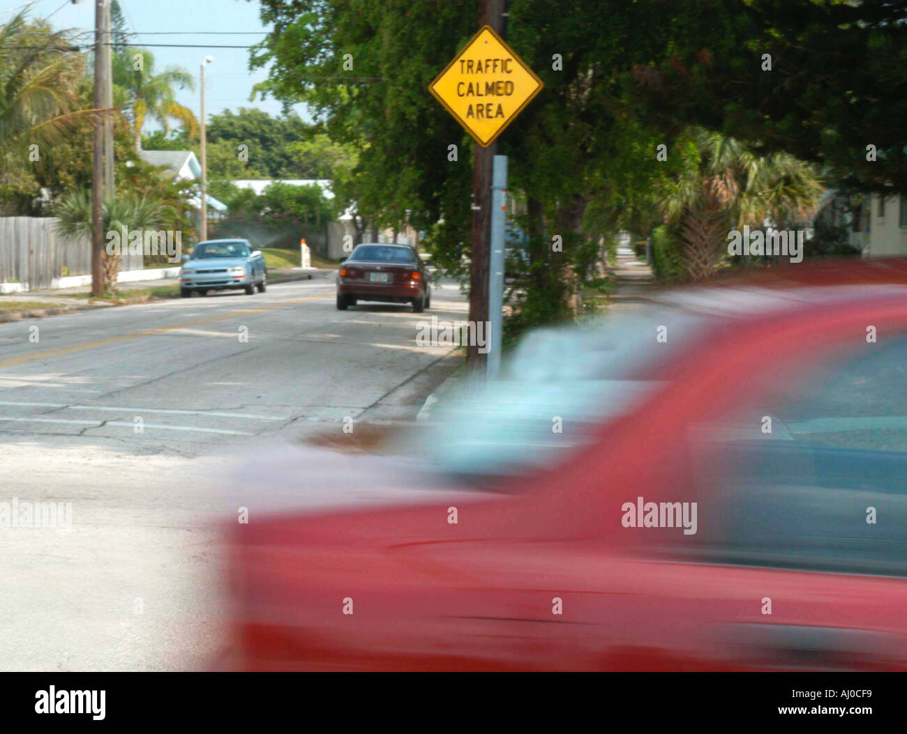 Ein rotes Auto fährt durch eine Vorstadt Kreuzung durch ein gelbes Verkehrsschild Verkehr beruhigt Leseecke Stockfoto