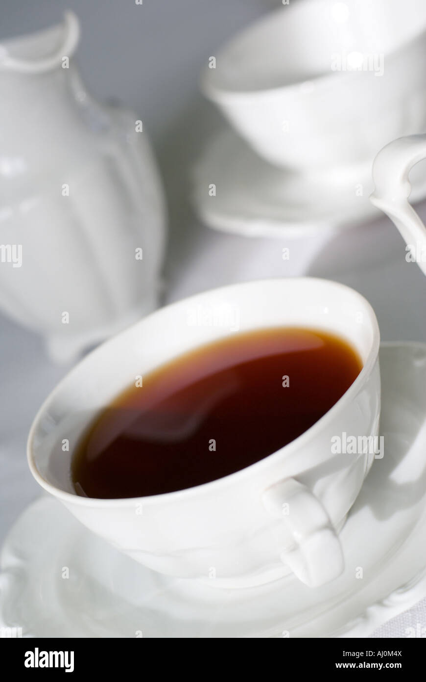 Tasse Tee Fokus nur in der Mitte der Tasse Kante und Porzellan Milchkännchen und noch eine Tasse hinter auf der weißen Tischdecke. Stockfoto