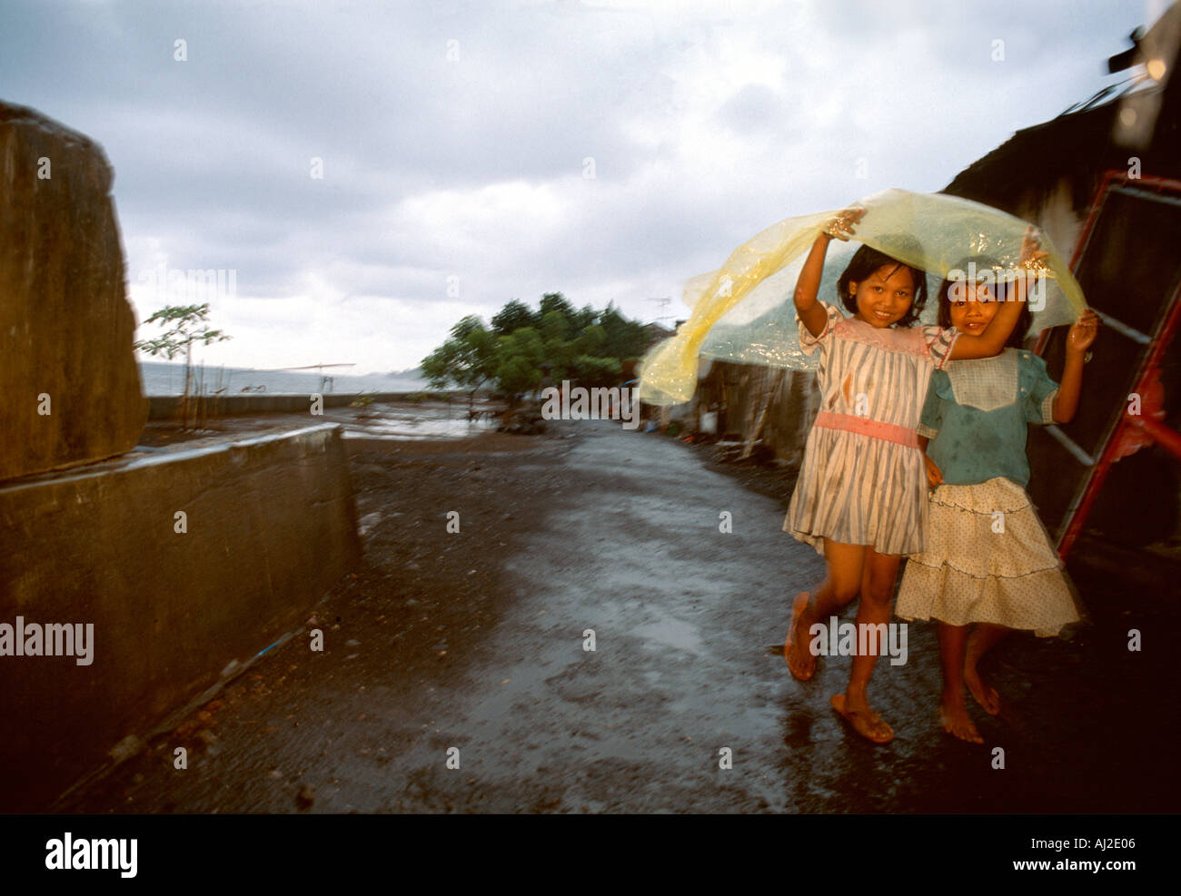Bali-Kinder im Regen. Zwei glückliche kleine Mädchen zu Fuß in der Monsun-Regen, Regenzeit in Singaraja, Bali, Indonesien. Stockfoto