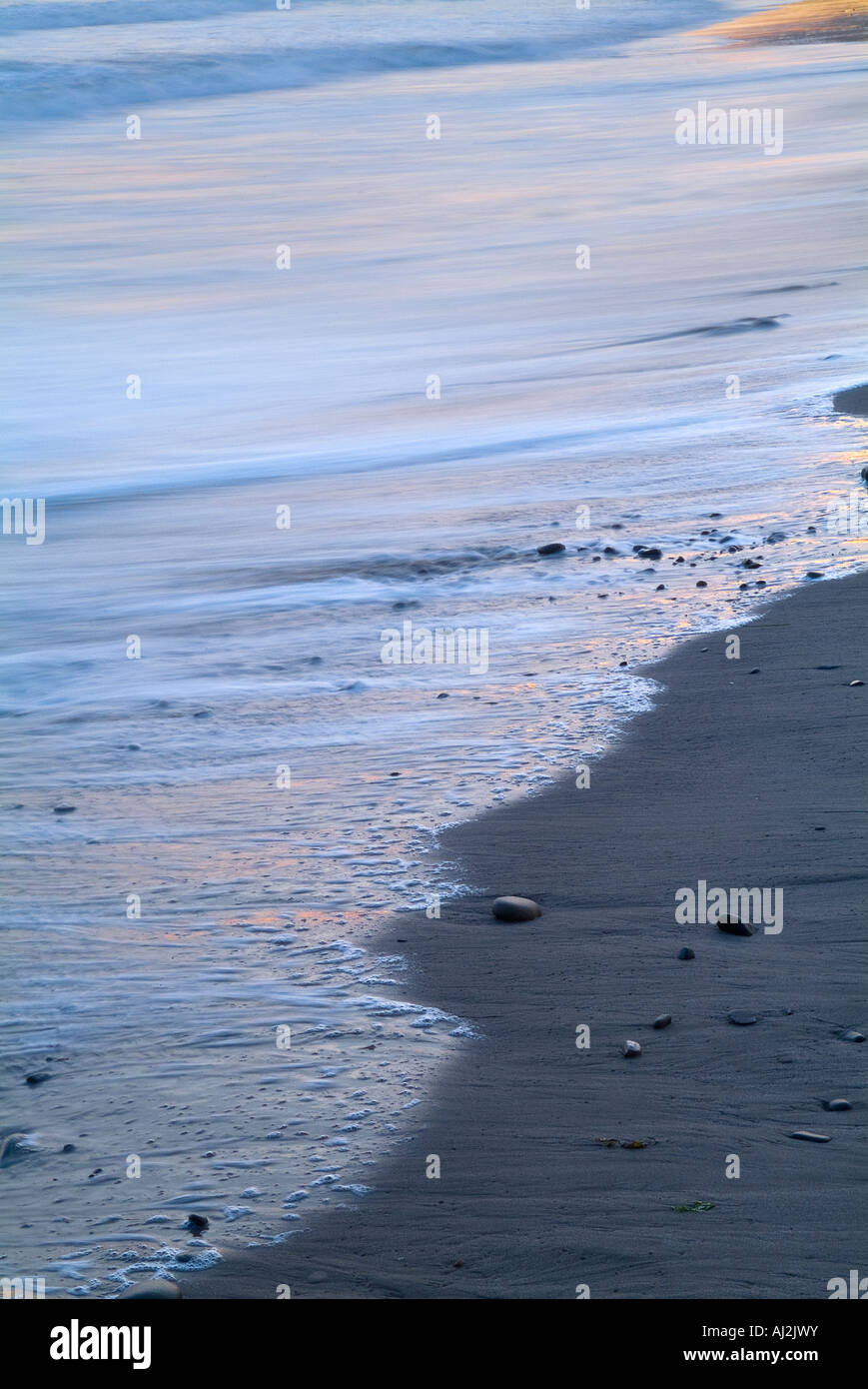 Ocean Wave Detail mit Kies und Steinen bei Sonnenuntergang Stockfoto