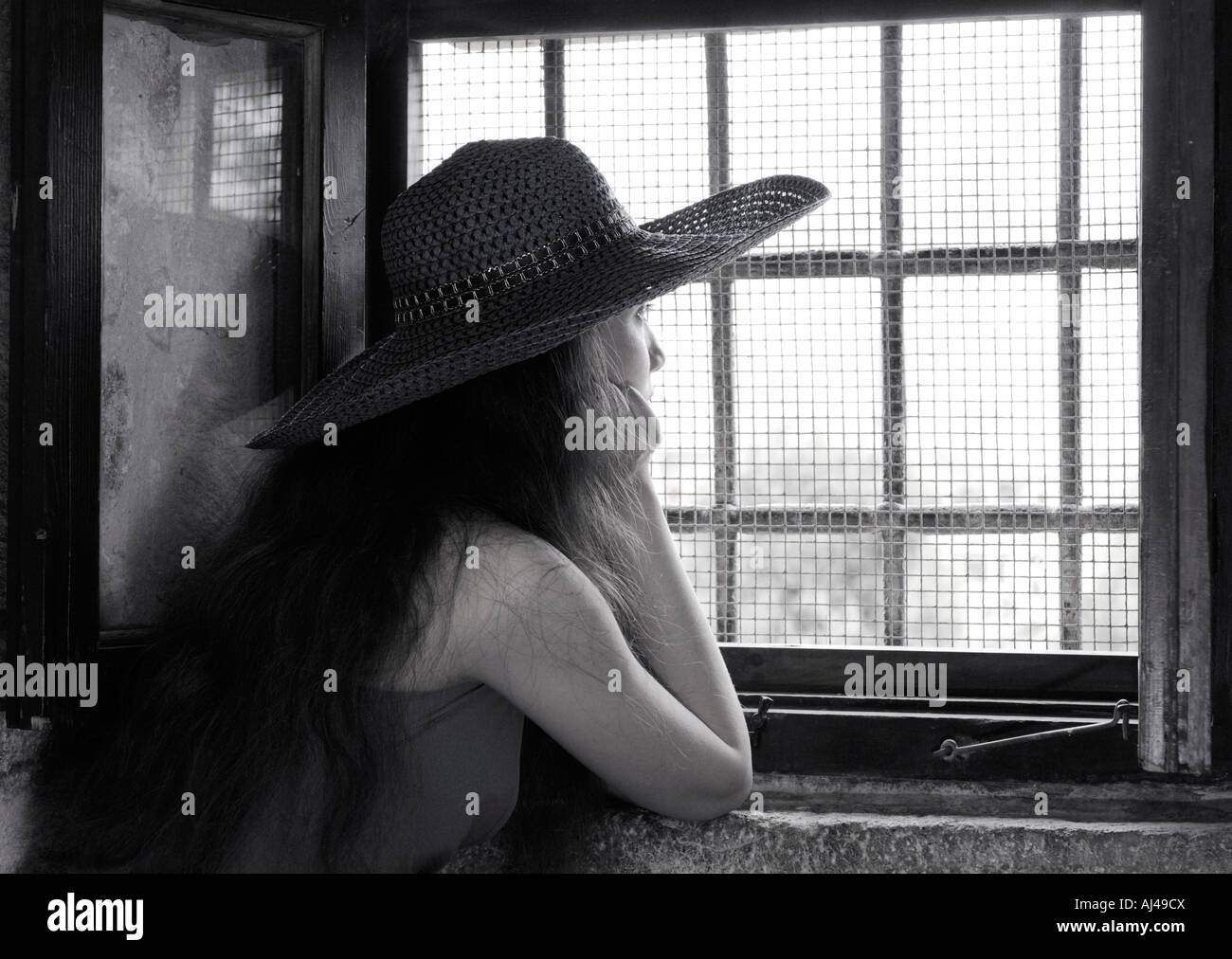 Junge Frau aus einem Fenster mit einem Rost mit Sonnenlicht daraus suchen Stockfoto