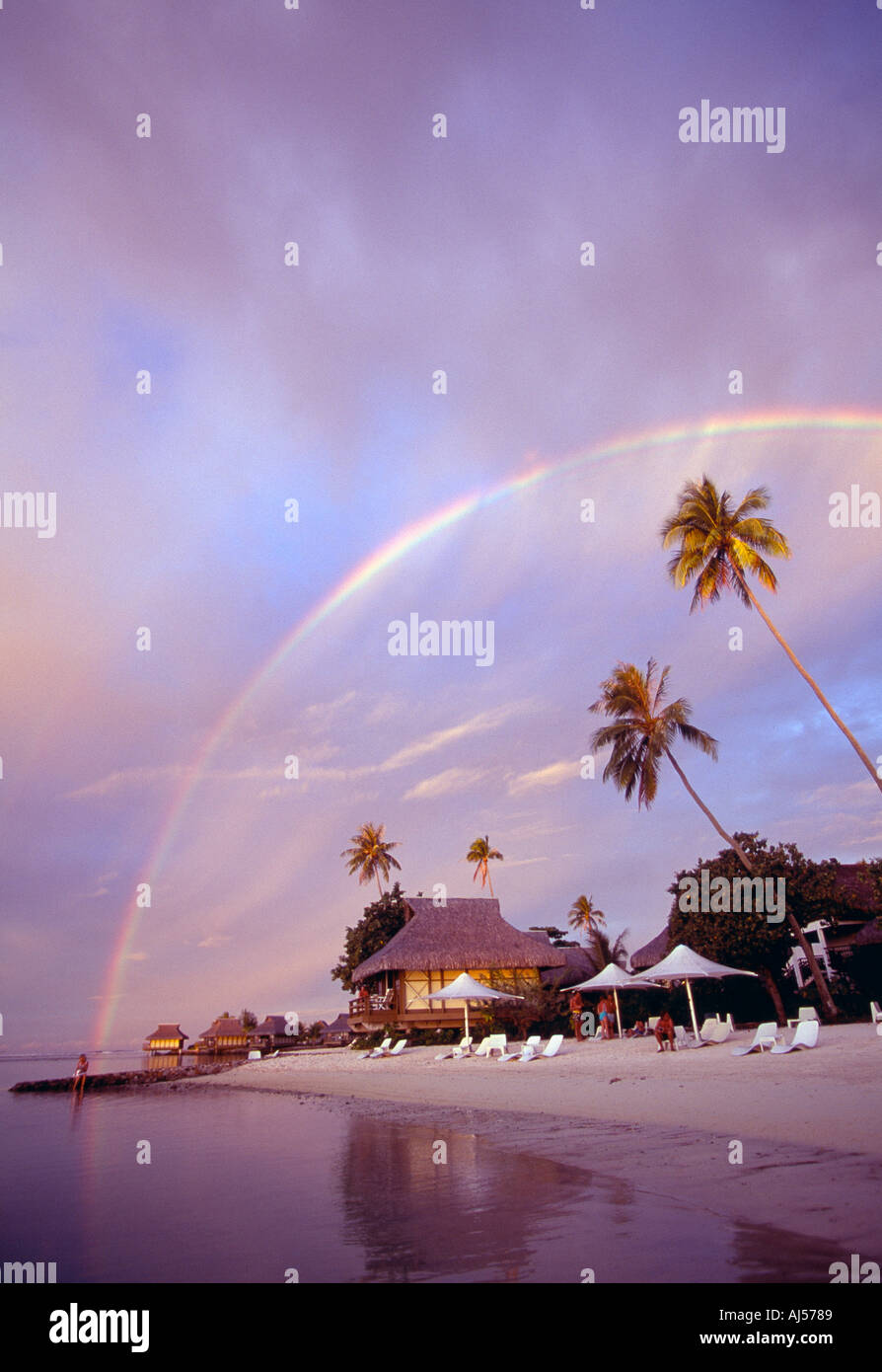 Französisch-Polynesien Moorea Regenbogen am Sonnenuntergang schwebt über Strand und bungalows Stockfoto