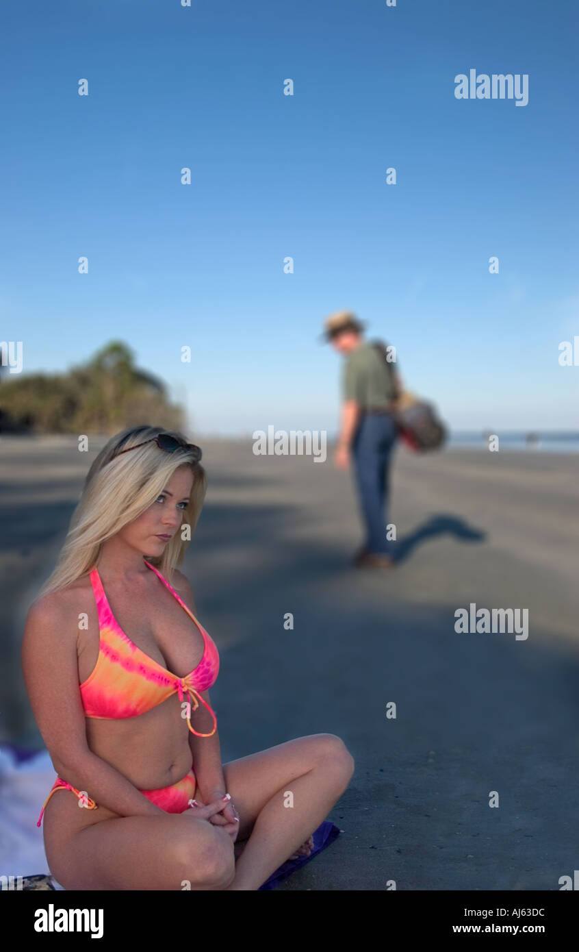 Kaukasische Mädchen 25-30 sitzen am Strand in Orange Bikini Pouts als Mann zu Fuß um Golf USA spielen Stockfoto