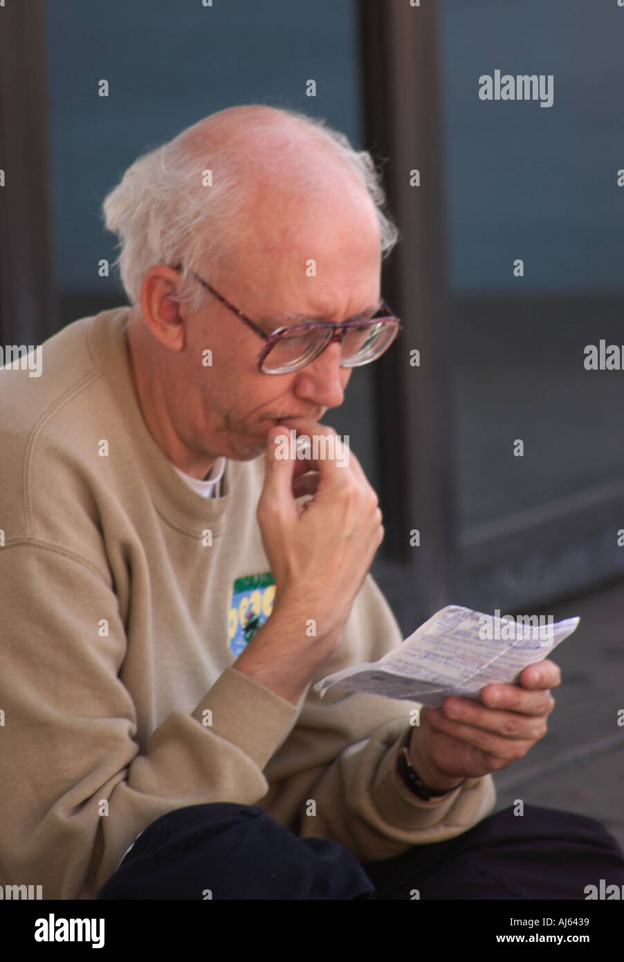 Älterer kaukasischer Mann mit weißem Haar und Brille, die in natürlichem Licht liest, USA. Stockfoto
