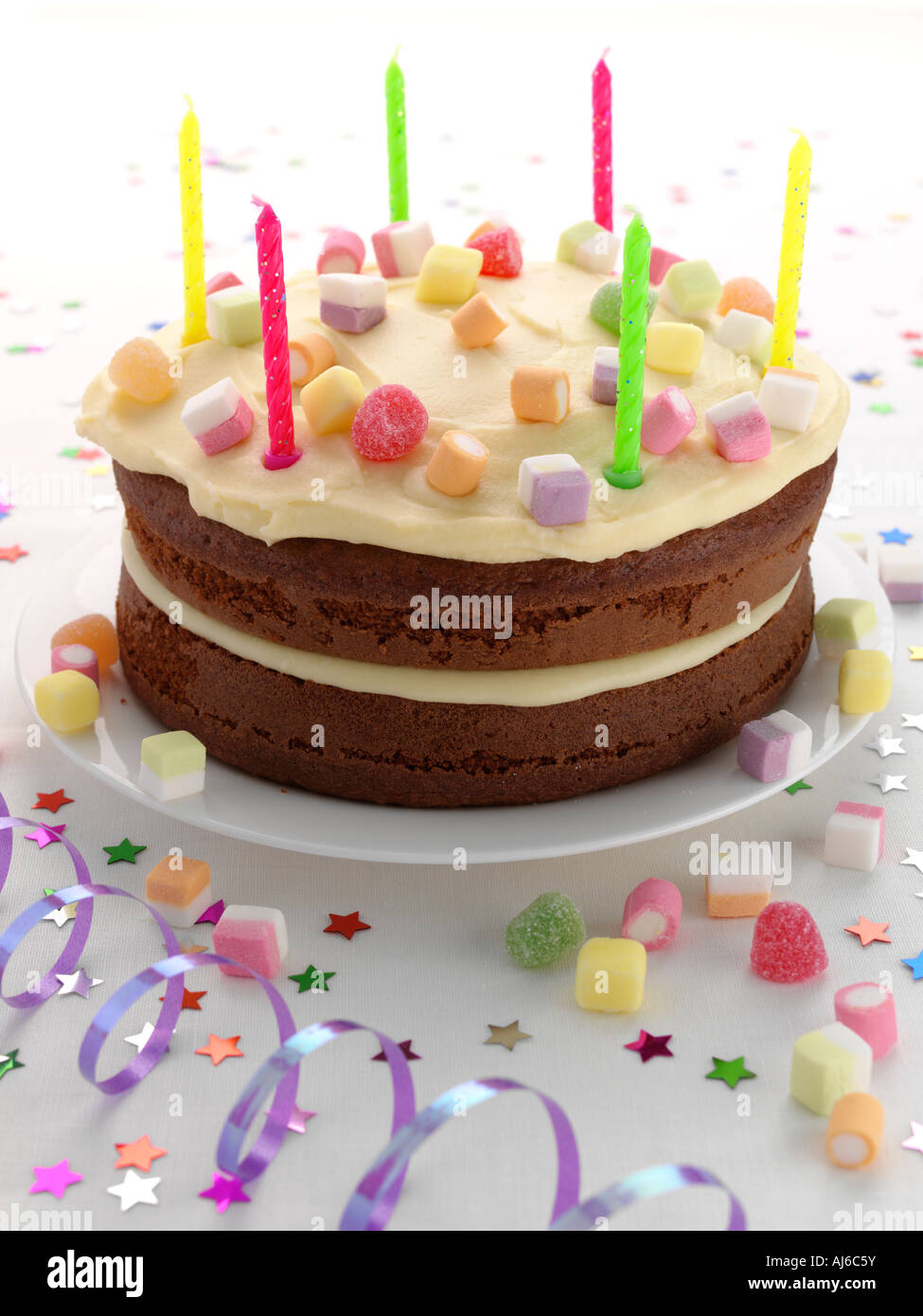 Eine Geburtstagstorte mit Kerzen und Luftschlangen auf weißem Hintergrund Stockfoto