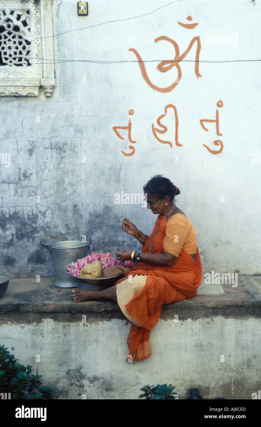 Weibliche Sadhu sitzt unter einem Om Symbol Nähen Reaths von Blumen außerhalb einer hinduistischen Tempel Gujarat Indien Stockfoto