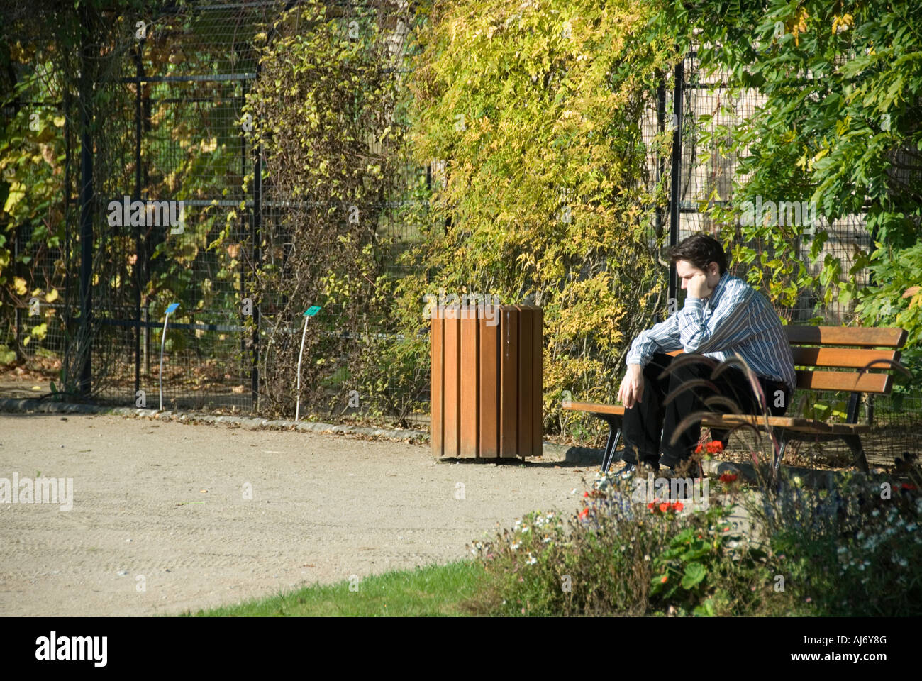 Stock Foto von einem jungen Mann allein sitzen tief in Gedanken versunken in einem öffentlichen Garten Stockfoto