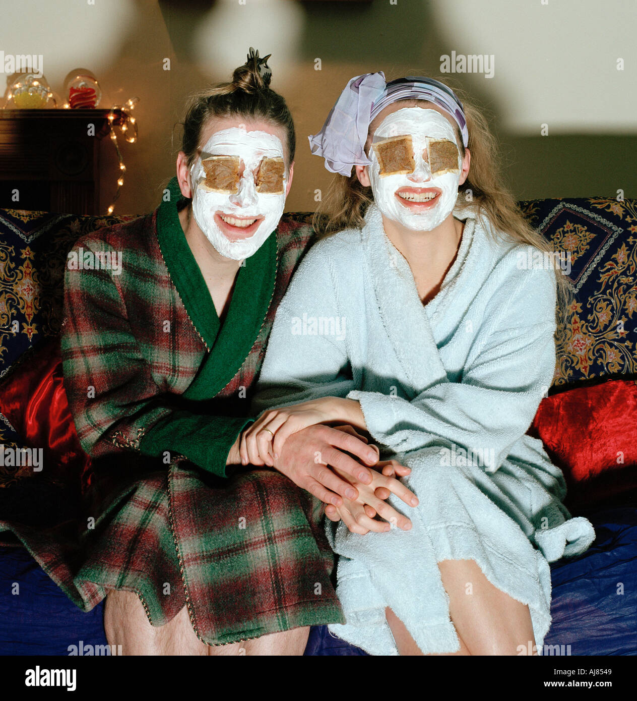 Paare mit Gesichtscreme und Teebeuteln im Wohnzimmer und Fernsehen Stockfoto