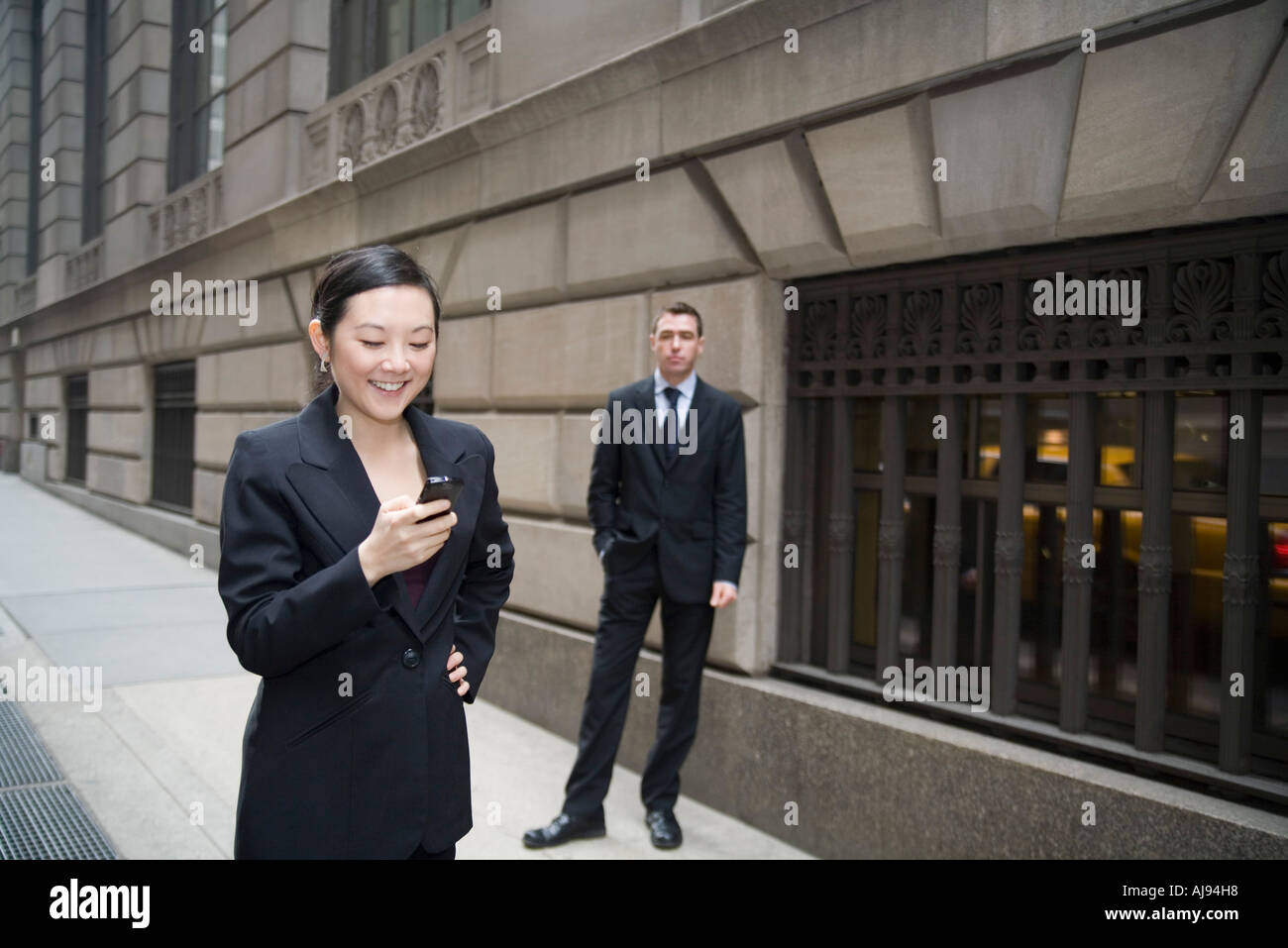 Geschäftsfrau mit Handy und Geschäftsmann wartet im Hintergrund Stockfoto